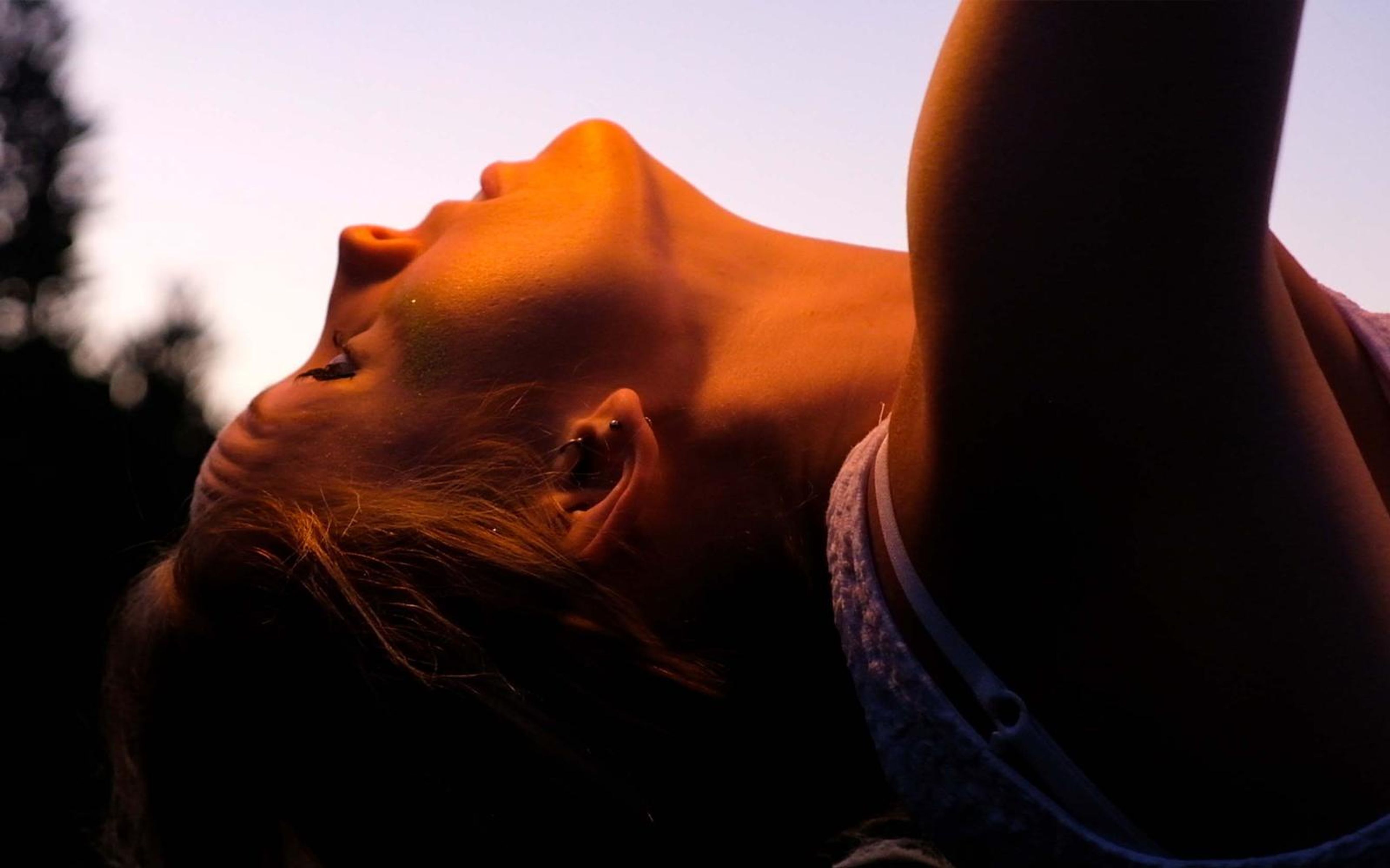 Woman's face tipped back with eyes closed, strong dusk light on her neck and chin