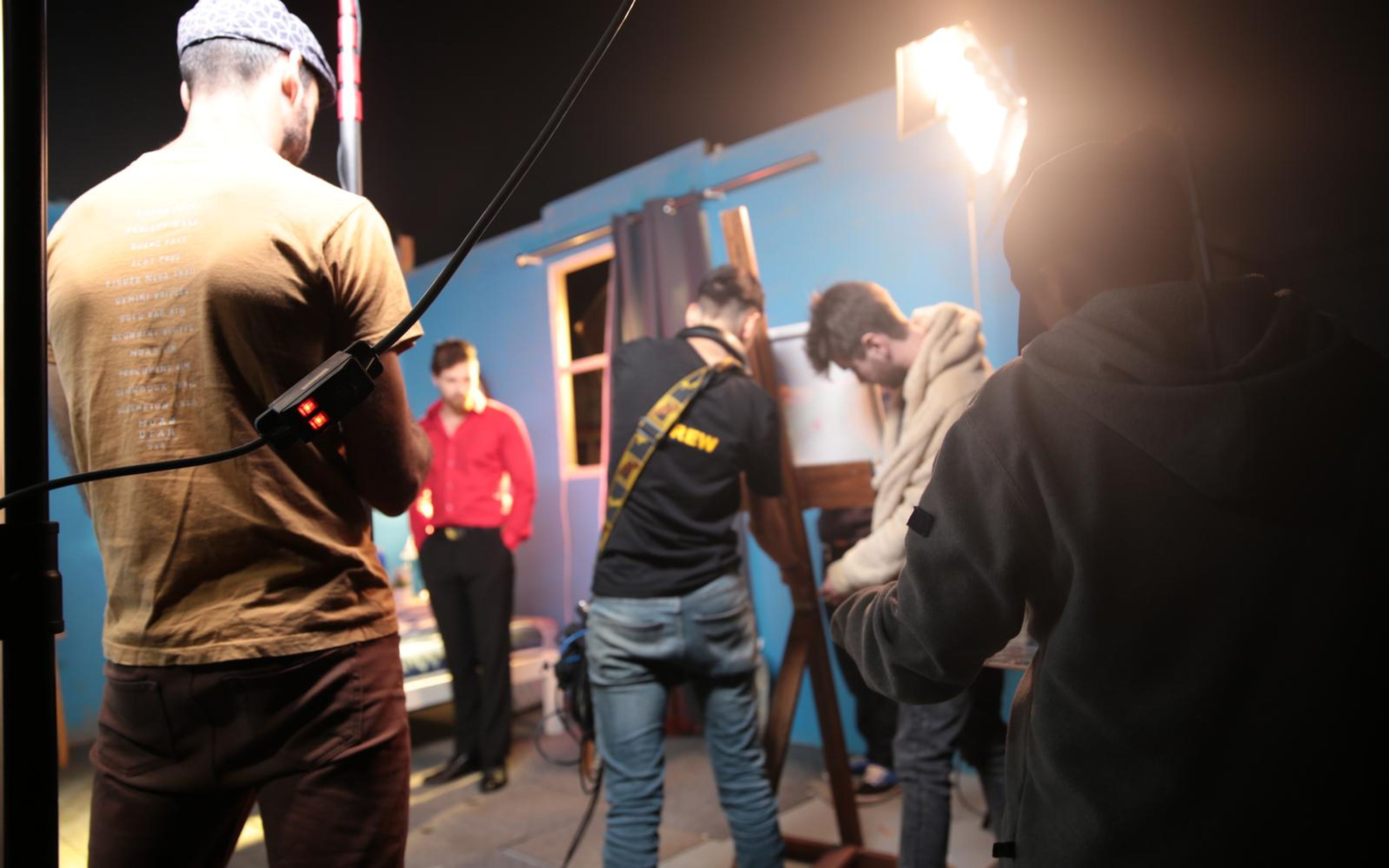Crew around an easel on a dark set lit by a bright lamp, with a boom pole held overhead