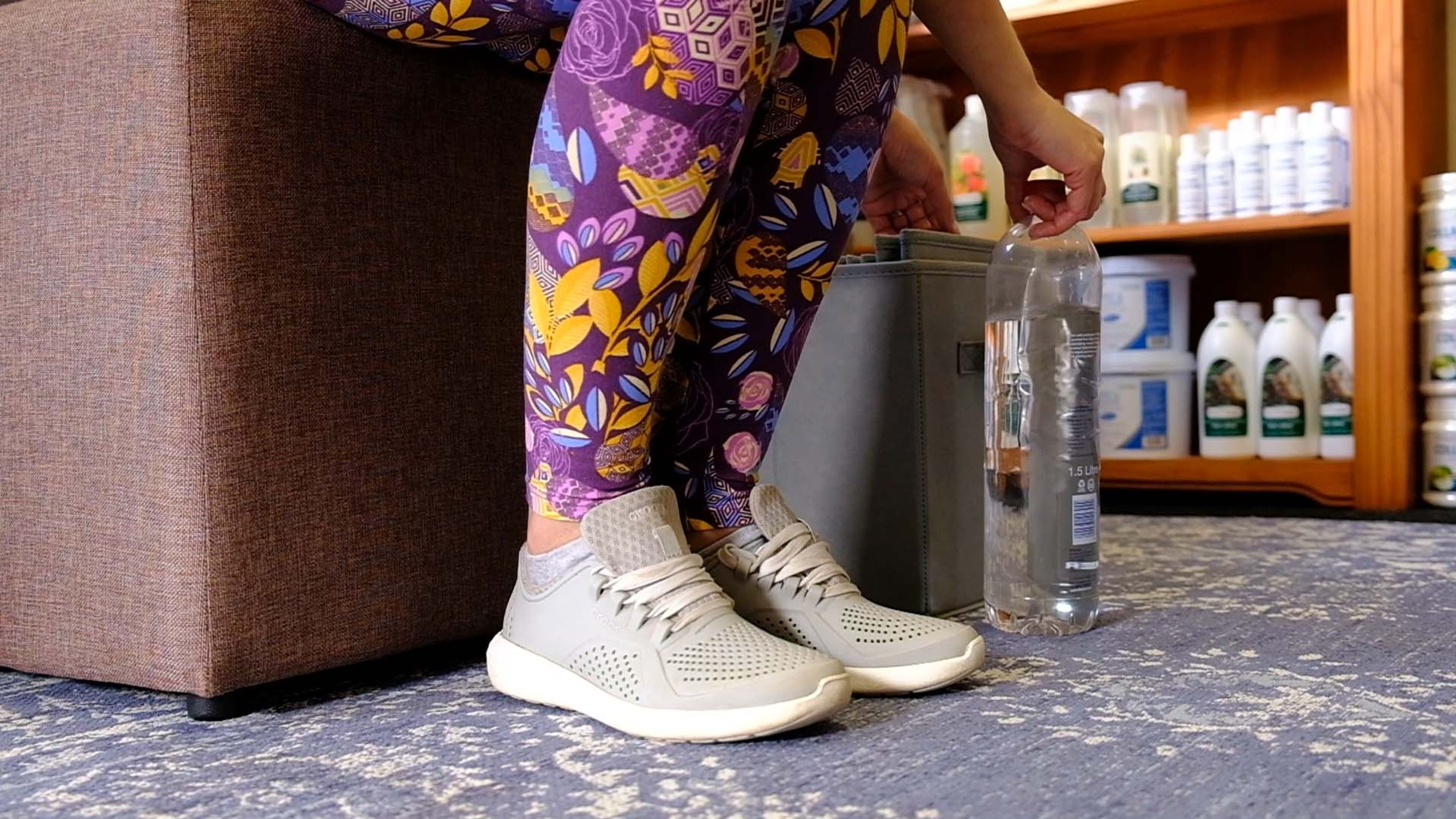 Client in purple floral leggings and sneakers standing beside a shelf of wellness products
