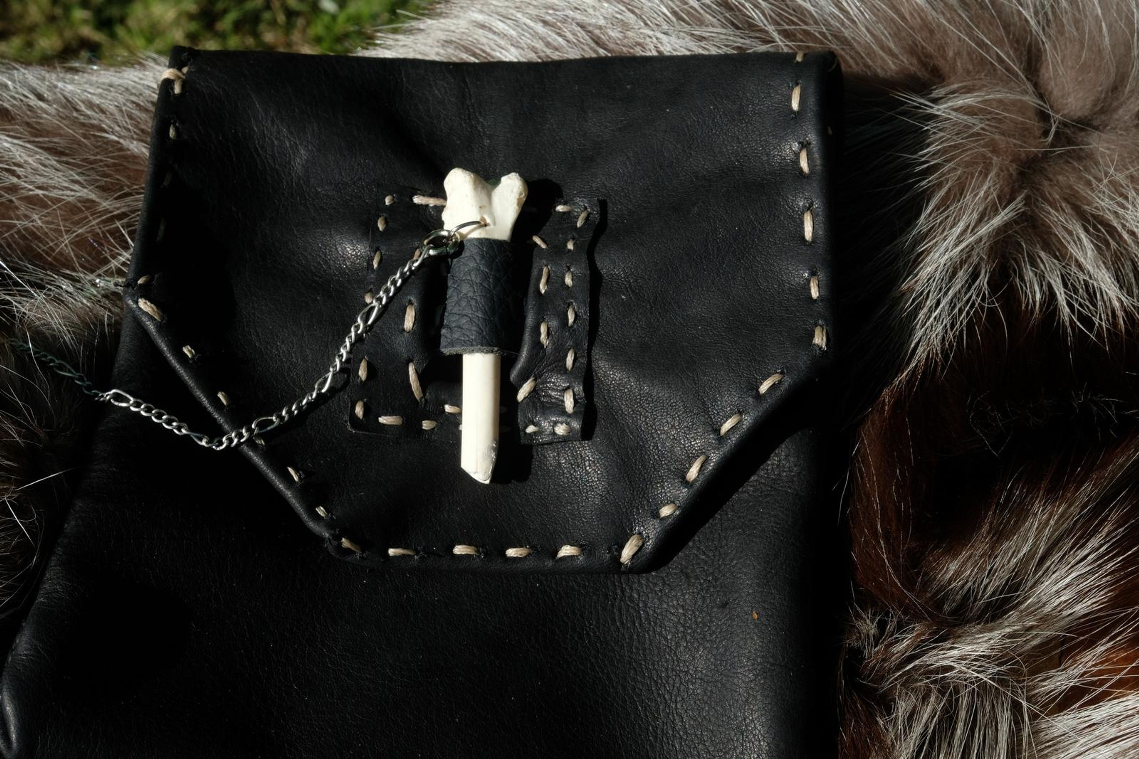 Black leather pouch with a bone toggle closure and chain on fur