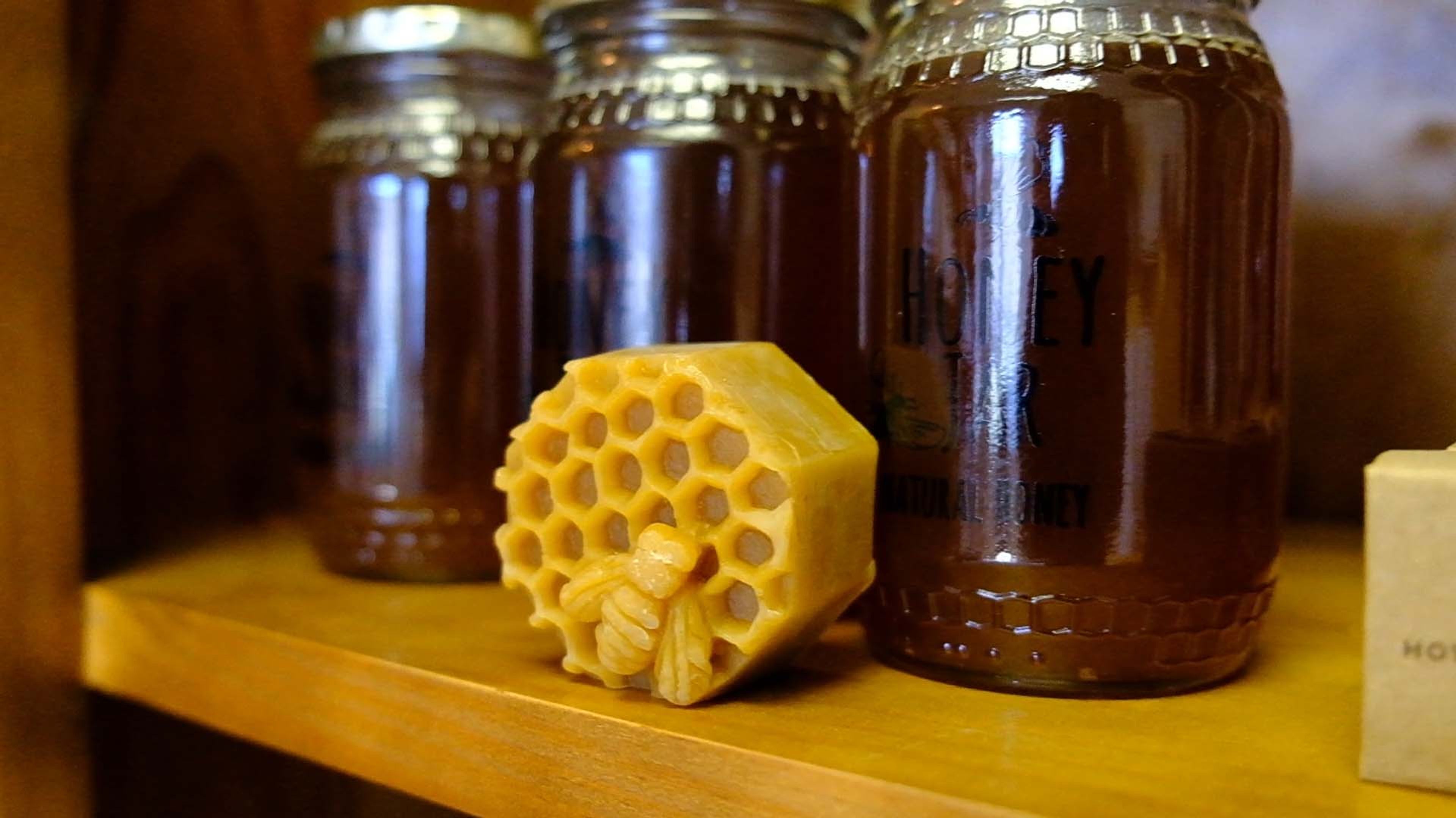 Jars of honey and a honeycomb on a wooden shelf