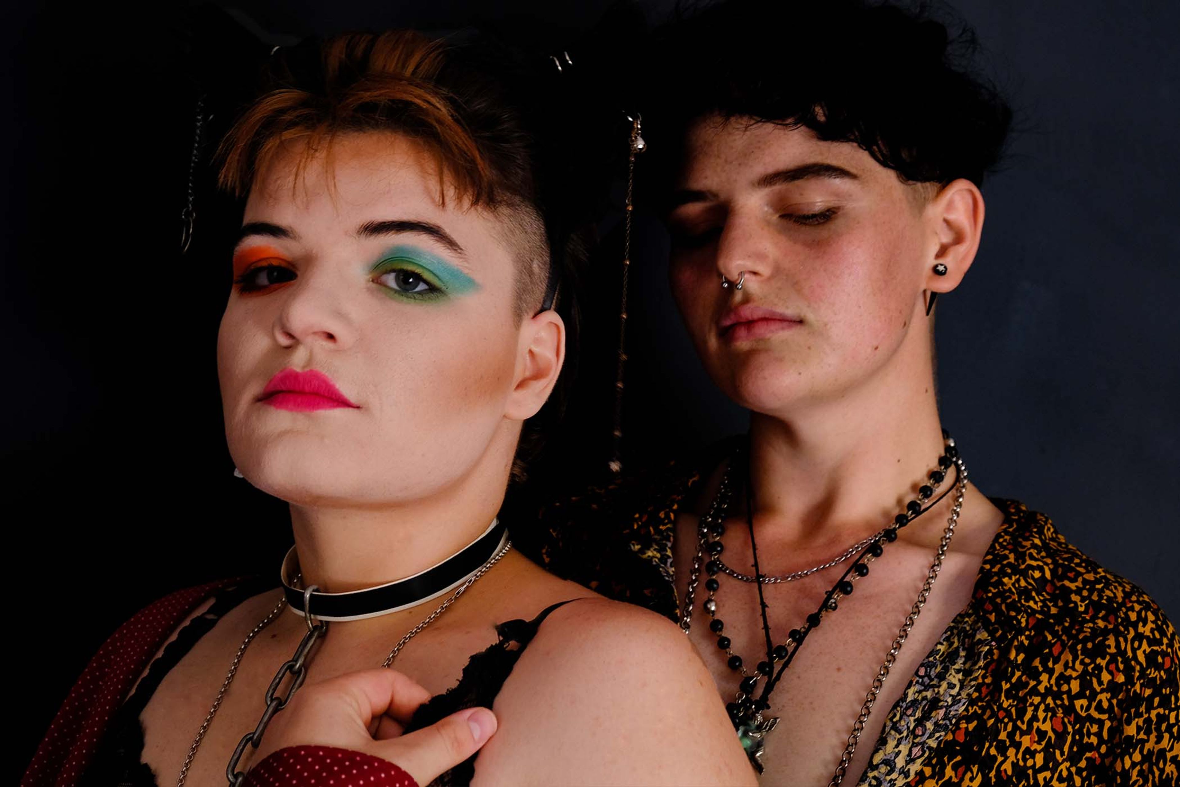 Portrait of a couple close together, colorful eye makeup, layered chain necklaces