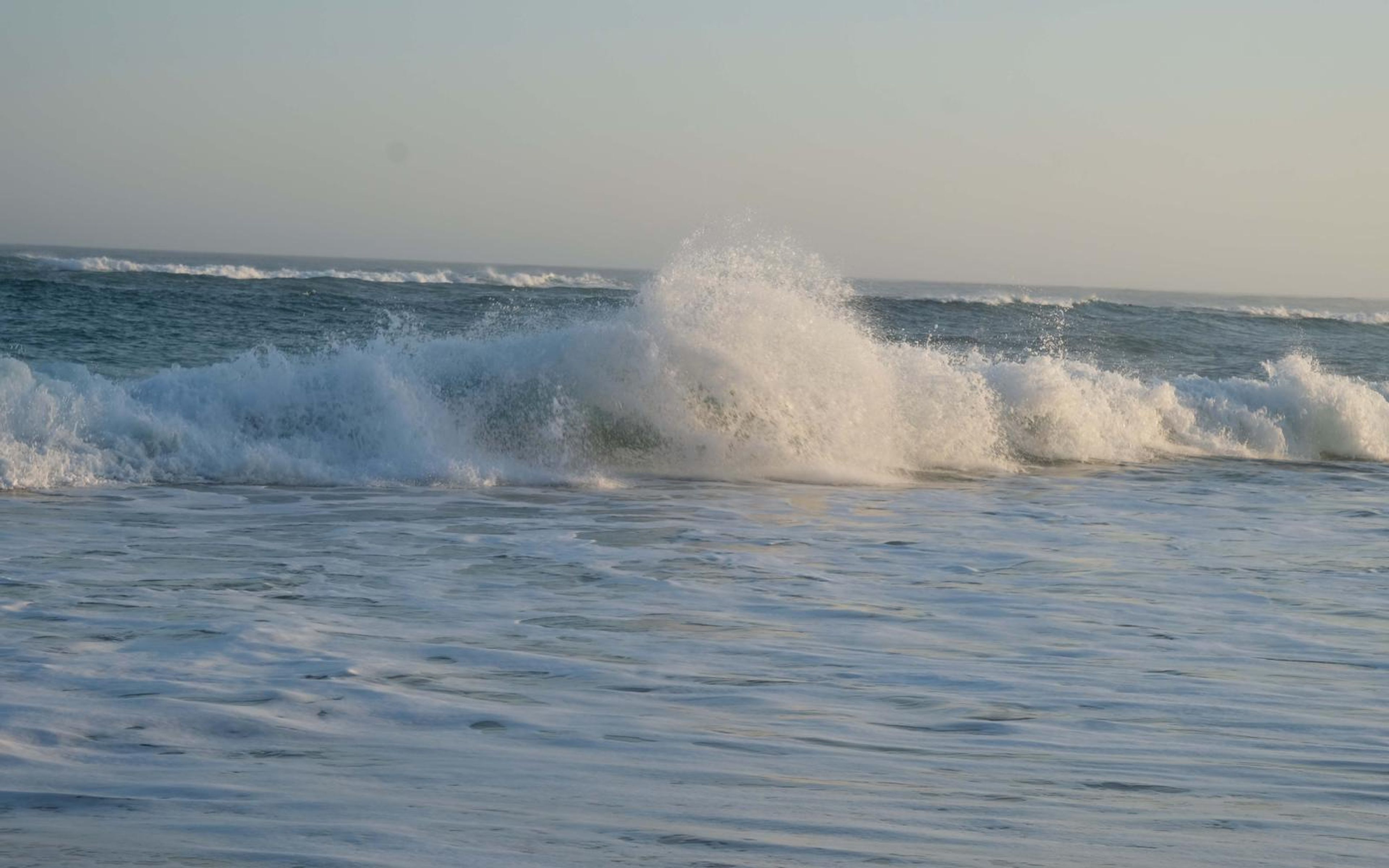 Wave breaking in a burst of spray against a pale evening sky