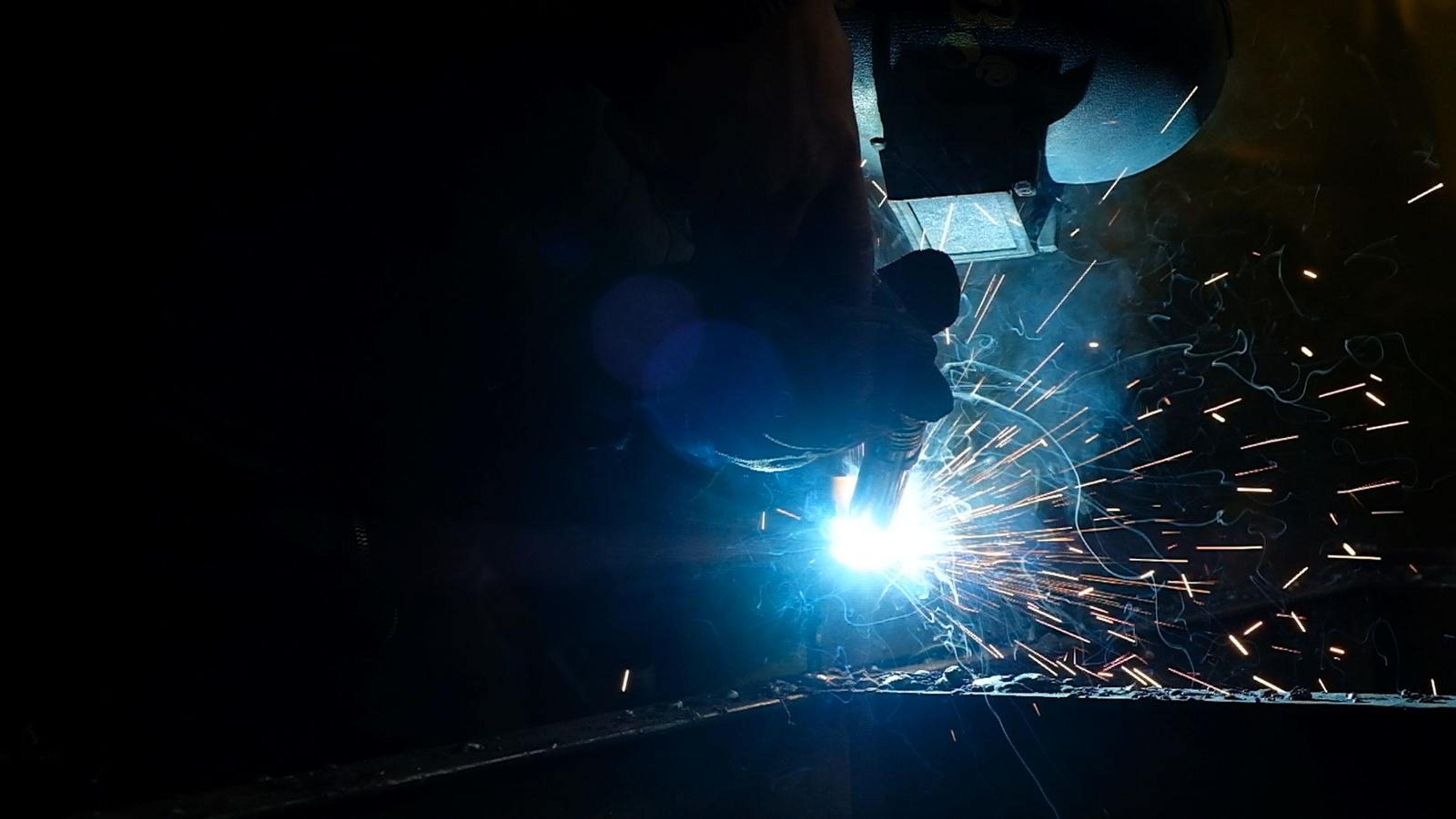 Welder's arc flaring in the dark with sparks streaming across the frame