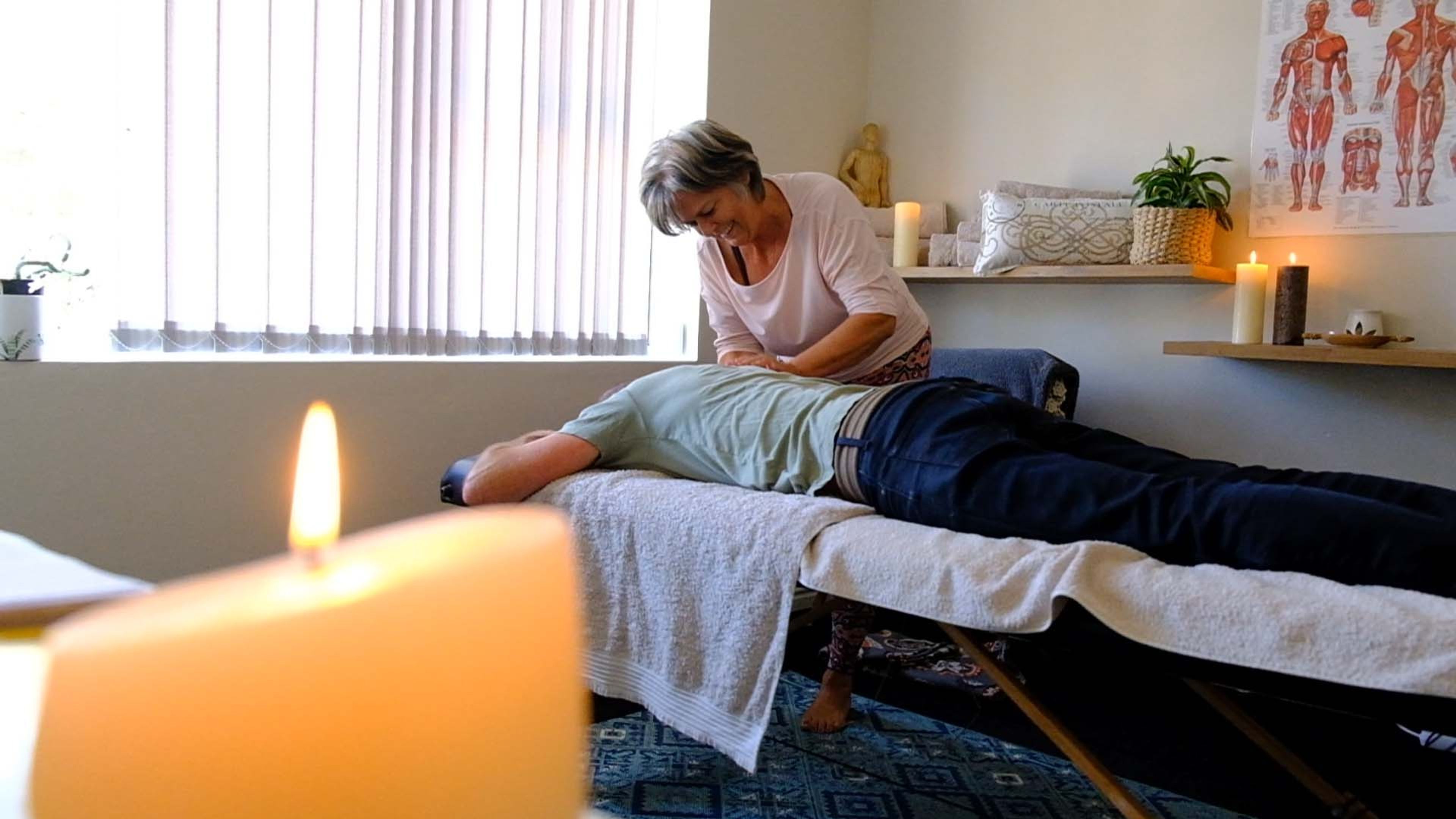 A therapist treating a client lying on a bed in a softly lit room, a candle in the foreground