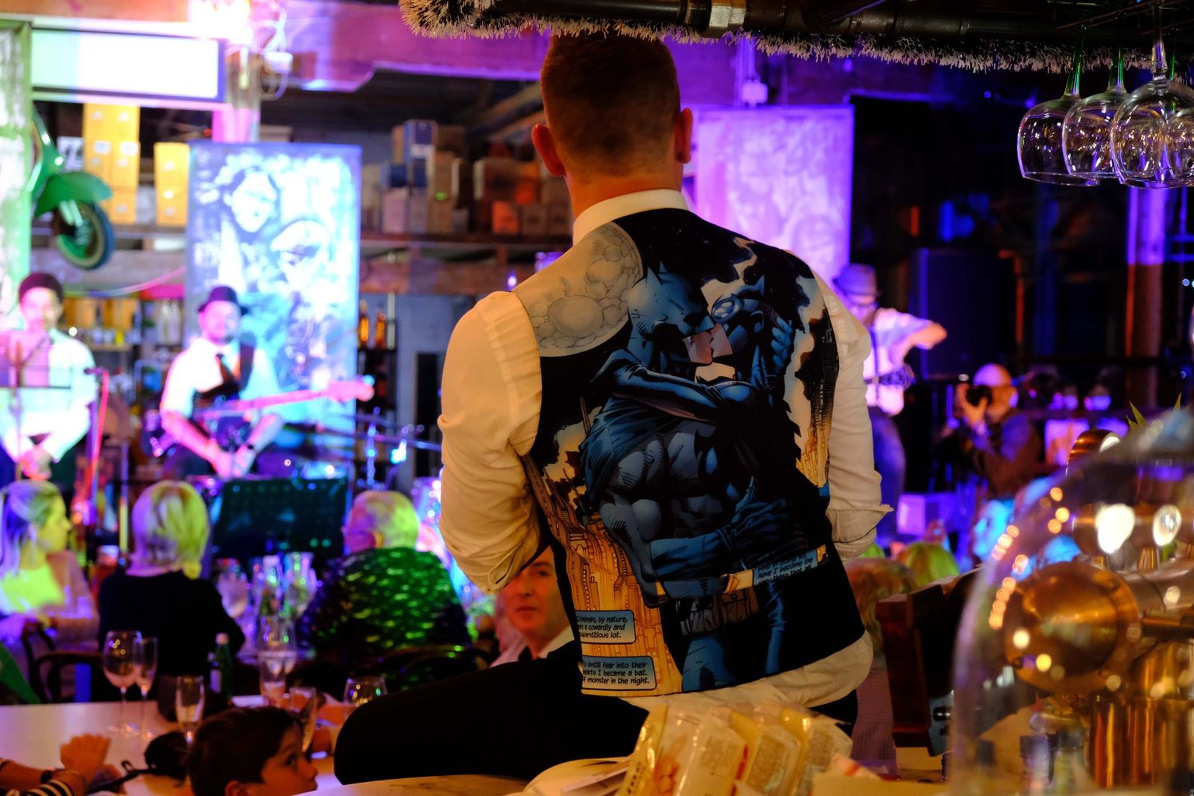 Singer in a printed waistcoat, seen from behind, facing the packed room