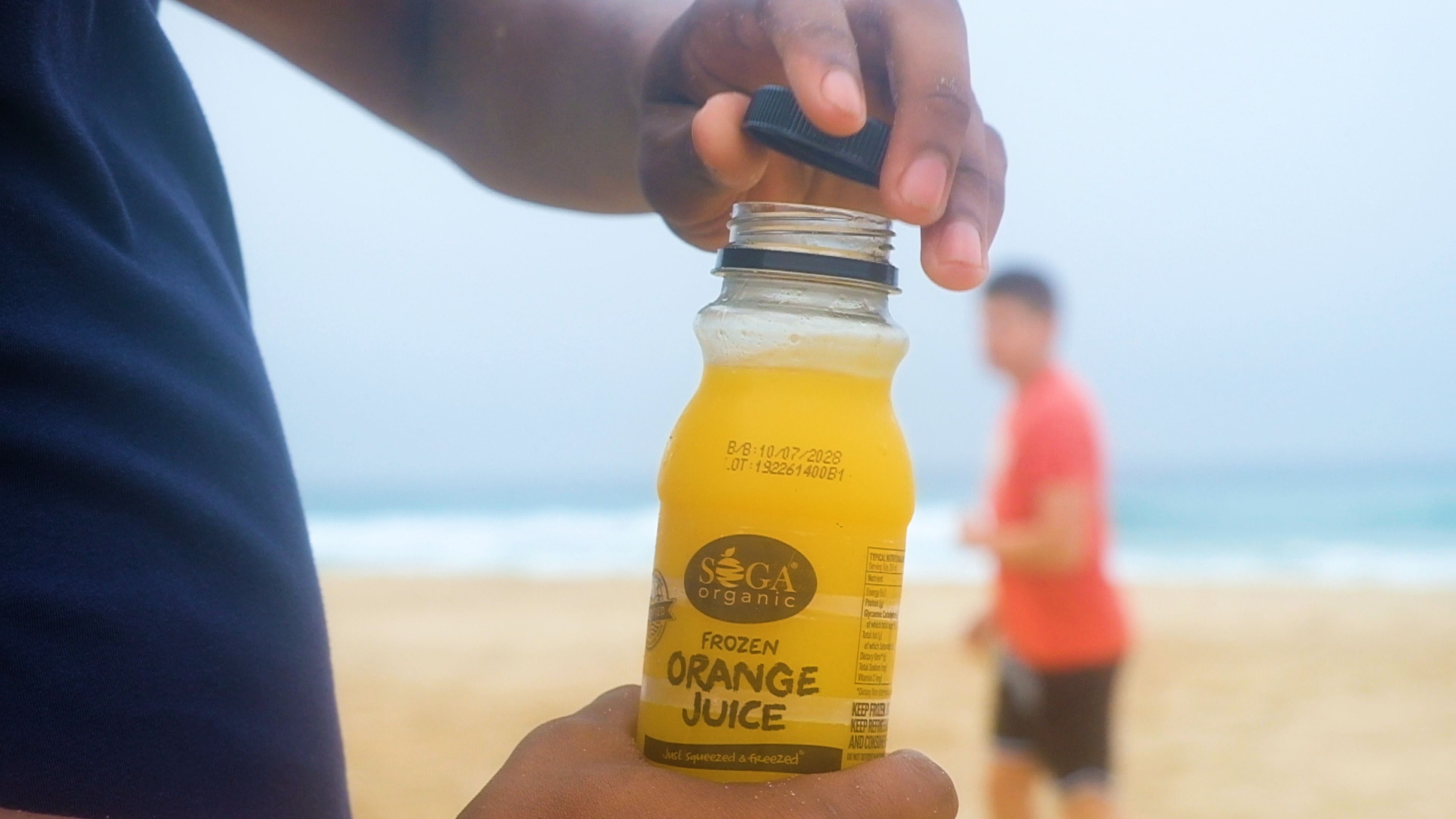 Hand opening a small bottle of orange juice on the beach