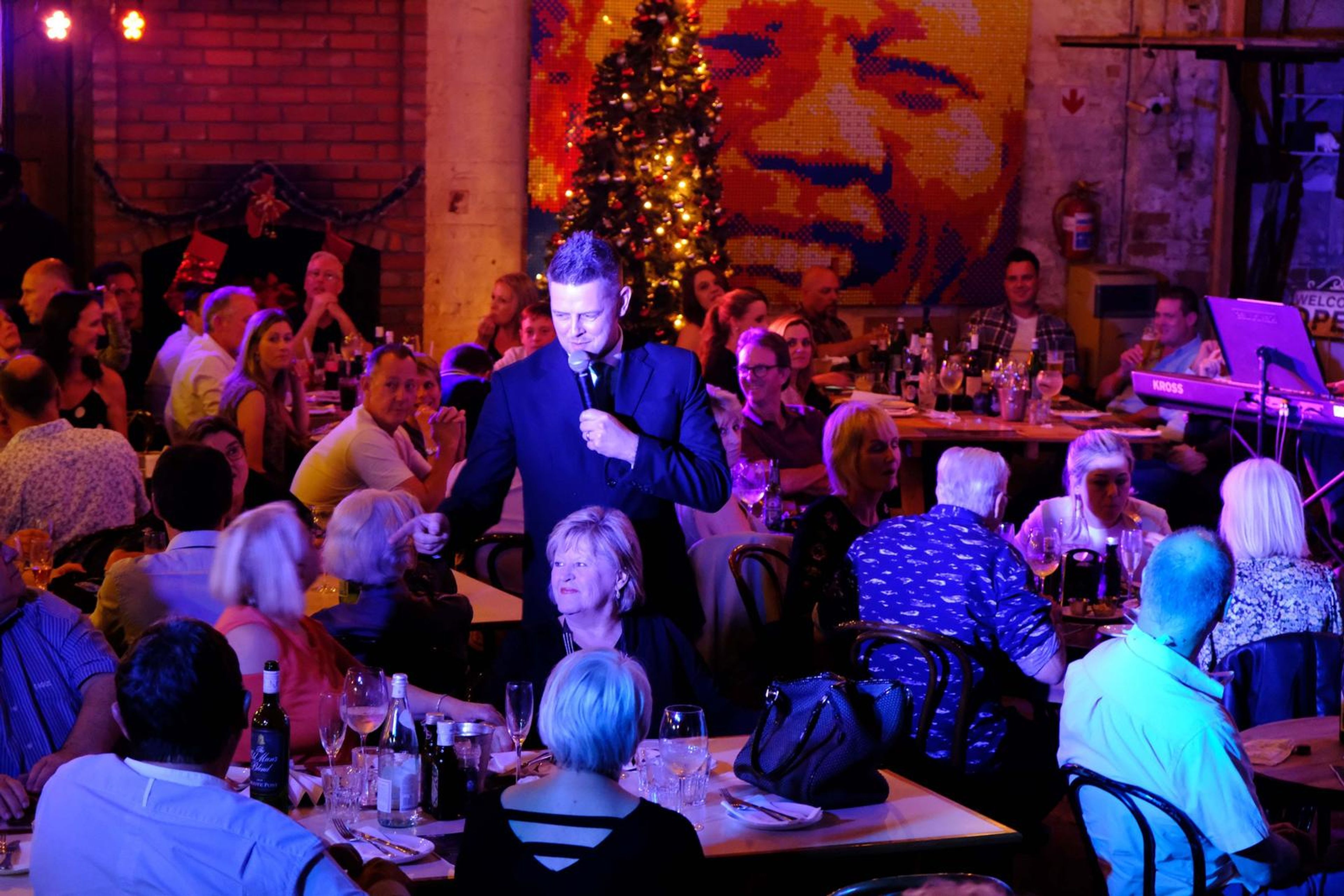 Wide view of the singer working the crowd in front of a Christmas tree and mural