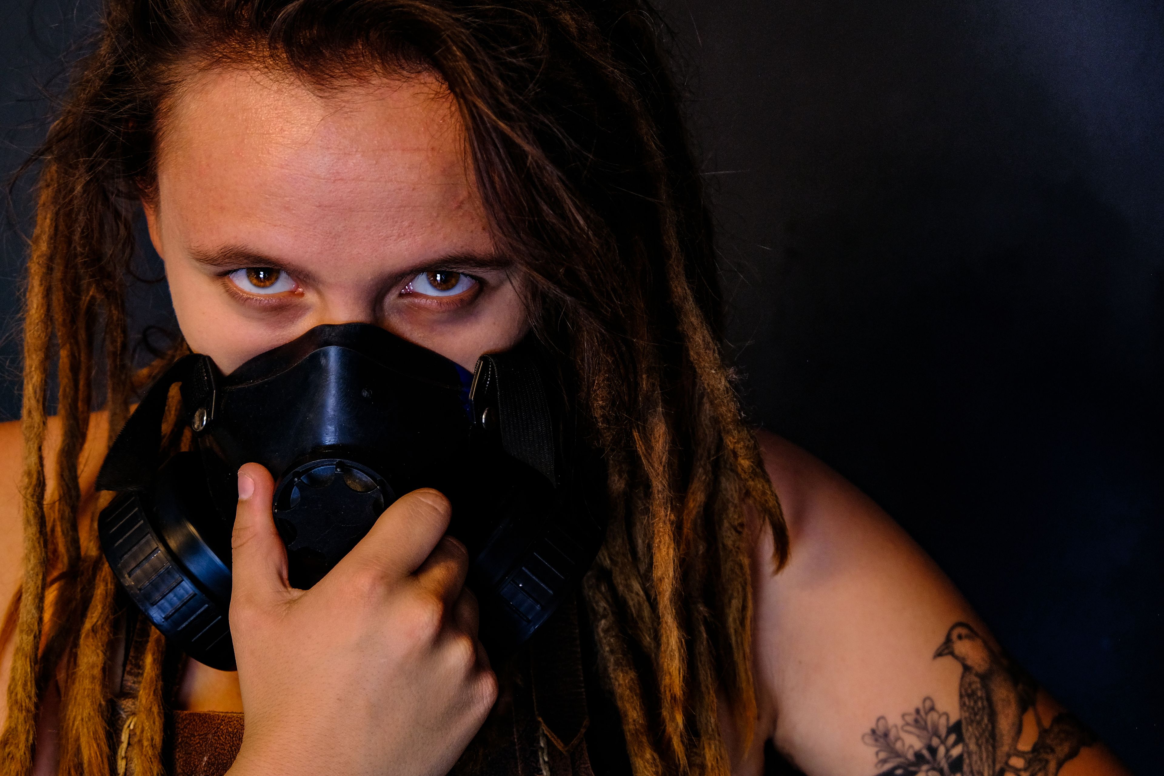Warm-toned close-up portrait, subject holding a gas mask to the face, direct eye contact