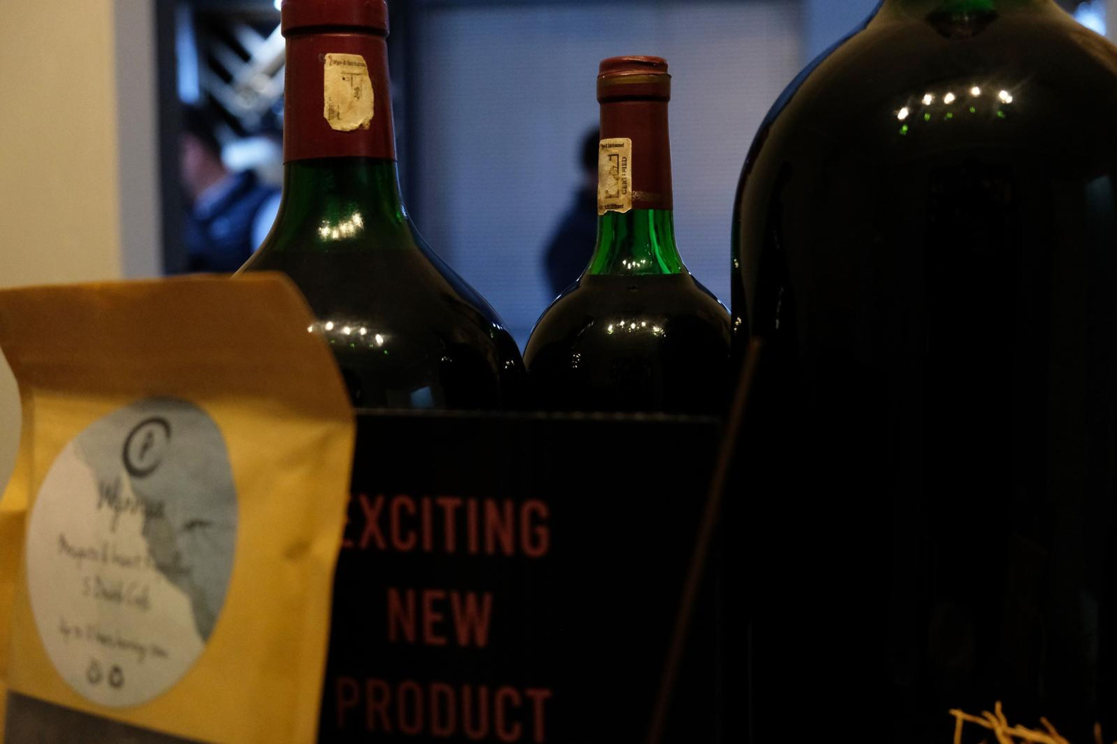Wine bottles and a bag of coffee beside an Exciting New Product sign