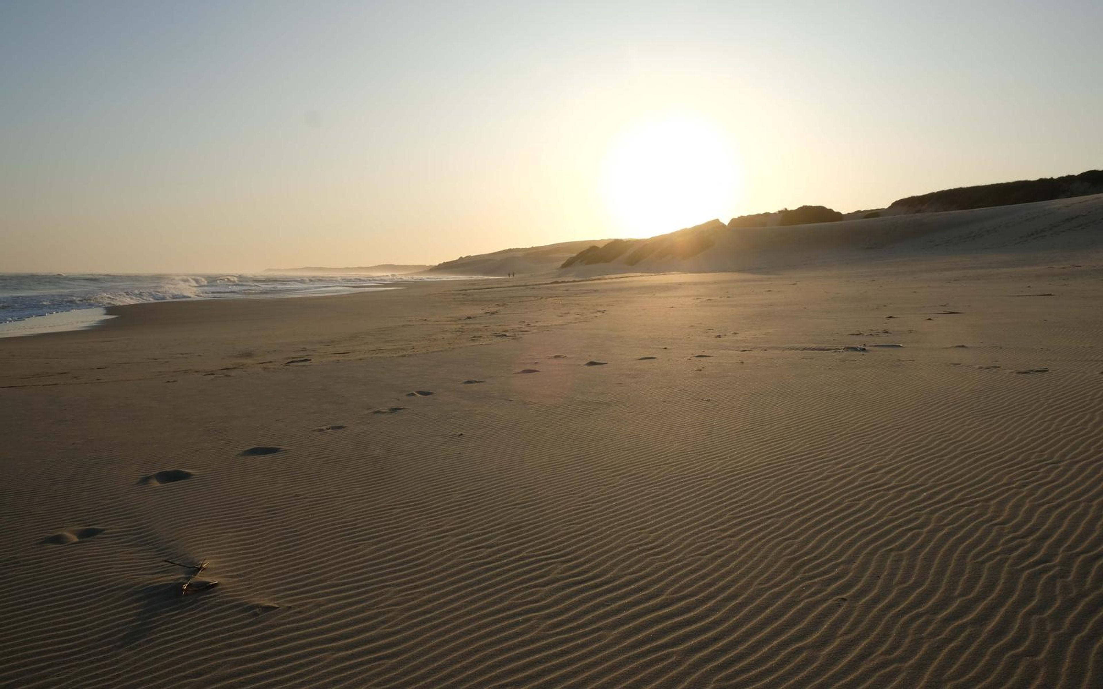 Sun setting over a long beach with footprints and fine ripples in the dark sand