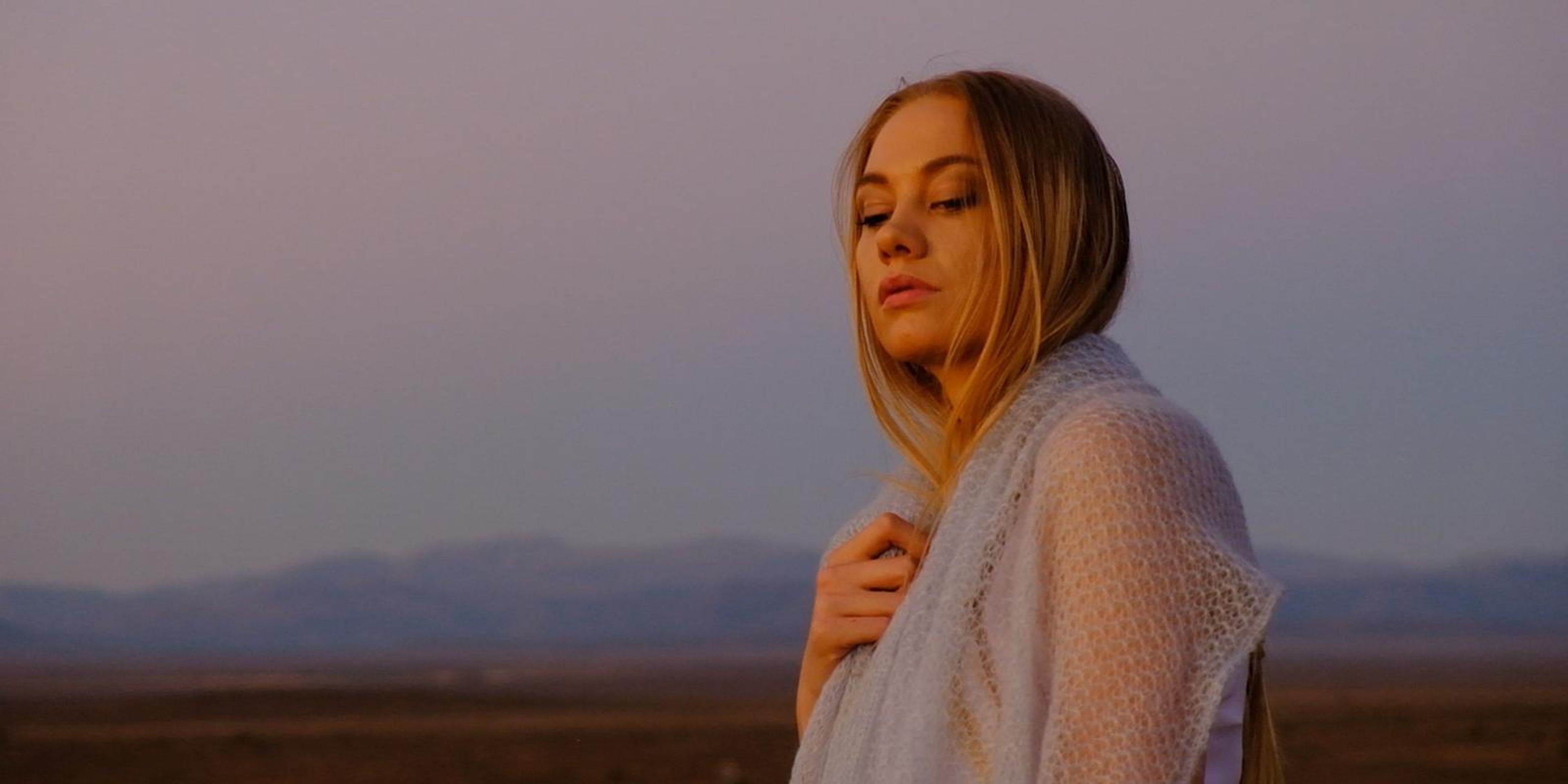 Model holding a cream mohair wrap against her chest at dusk