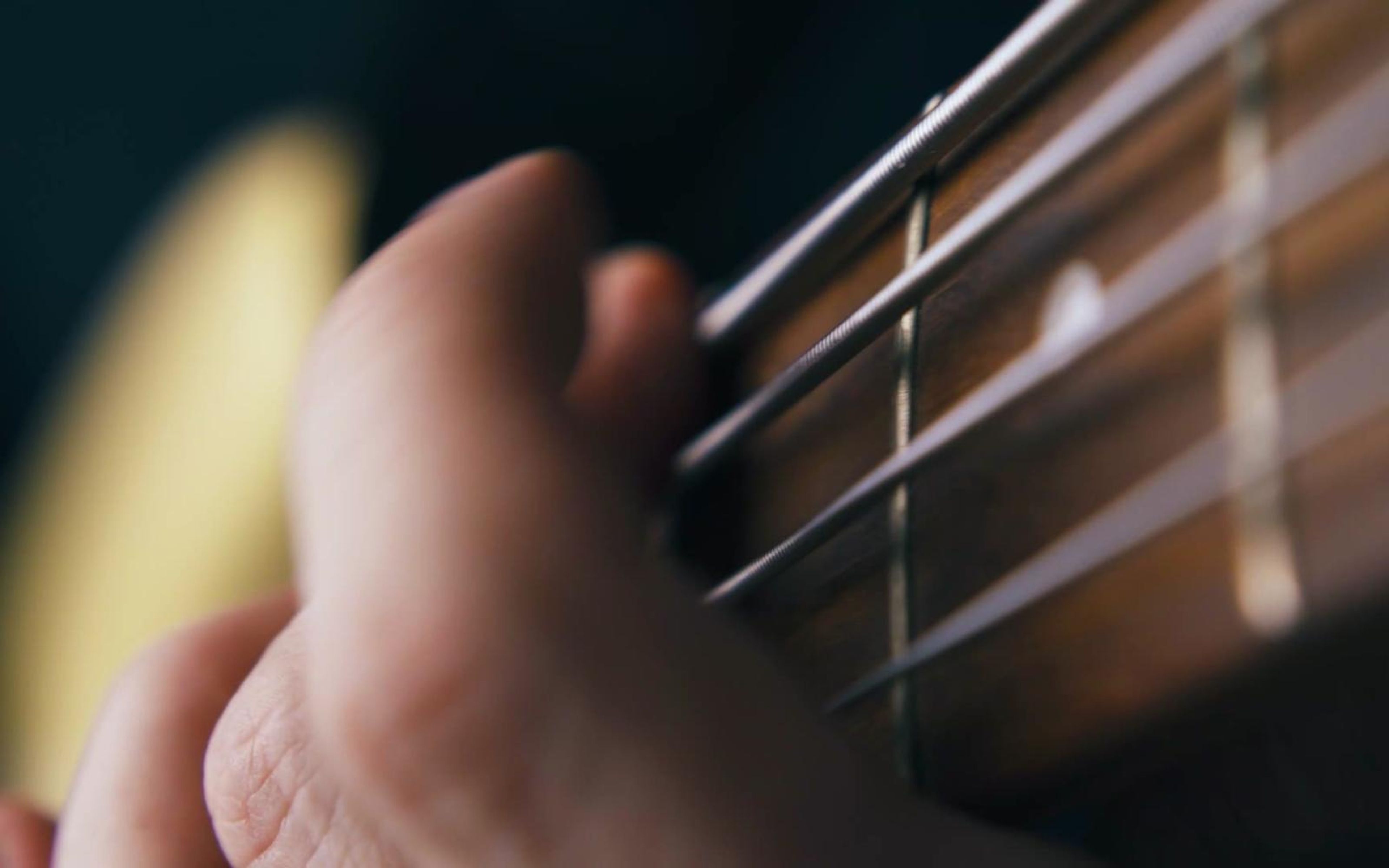 Close-up of a hand pressing guitar strings on a wooden fretboard, shallow focus