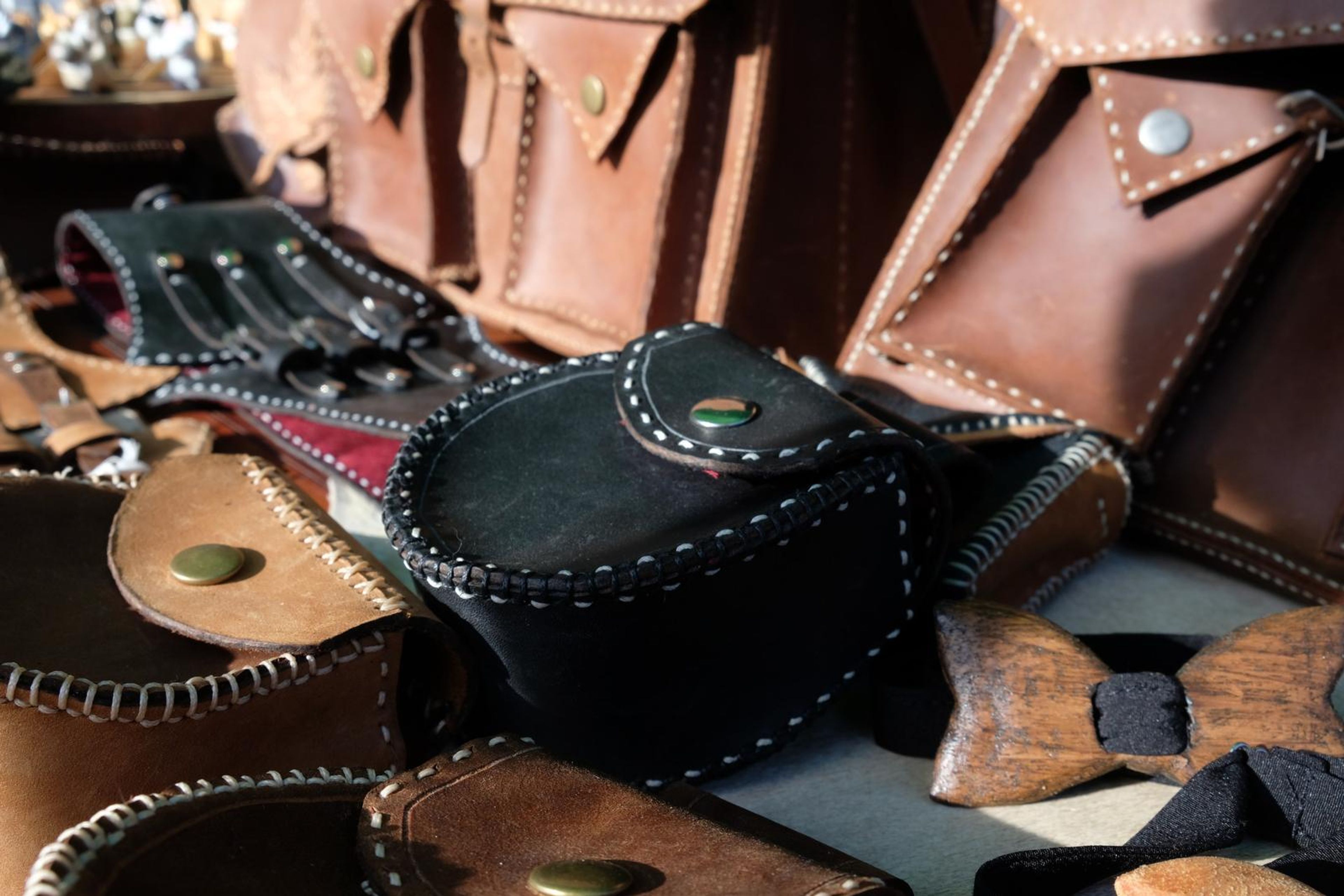 Black leather pouch with brass stud among corset belts and a carved bow tie