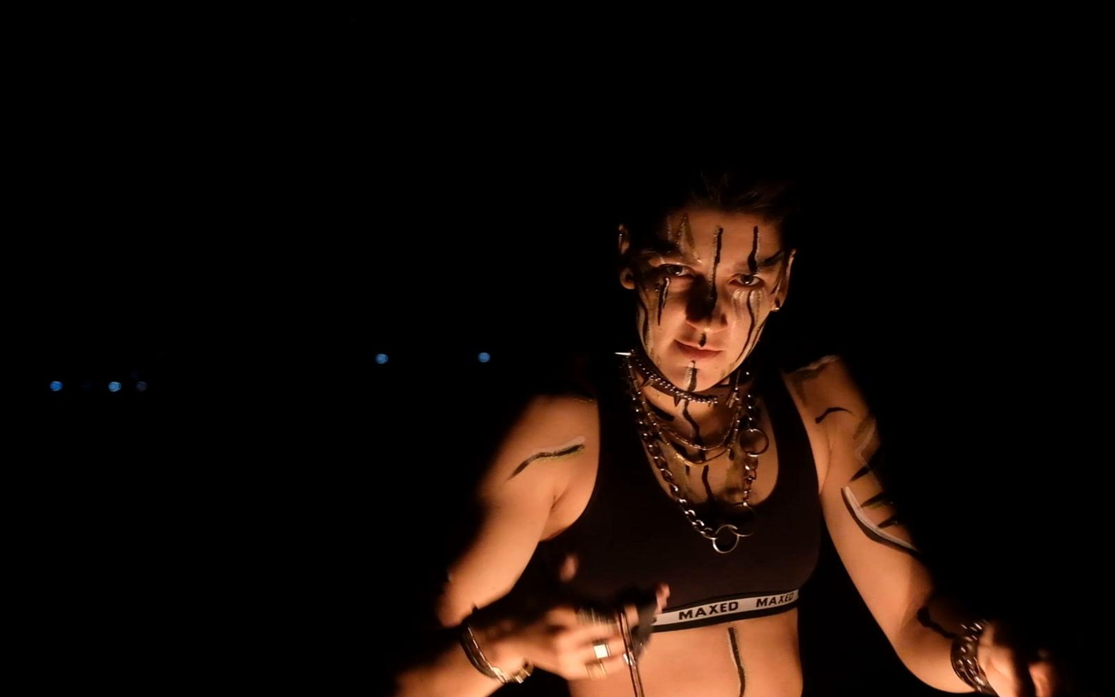Face-painted performer looking into the camera with fire poi lighting his chest