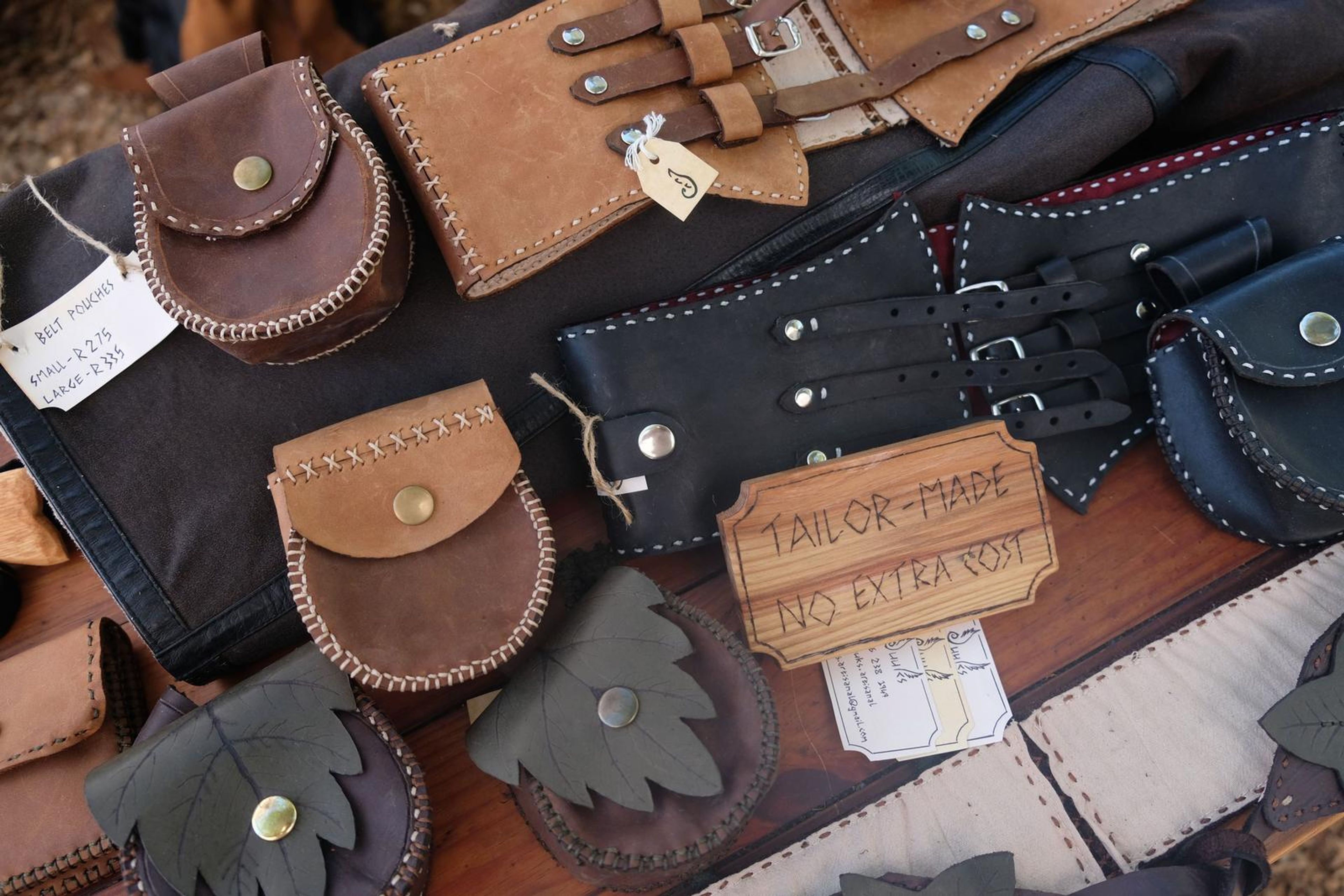 Table of handmade leather pouches and corset belts with a Tailor-Made sign