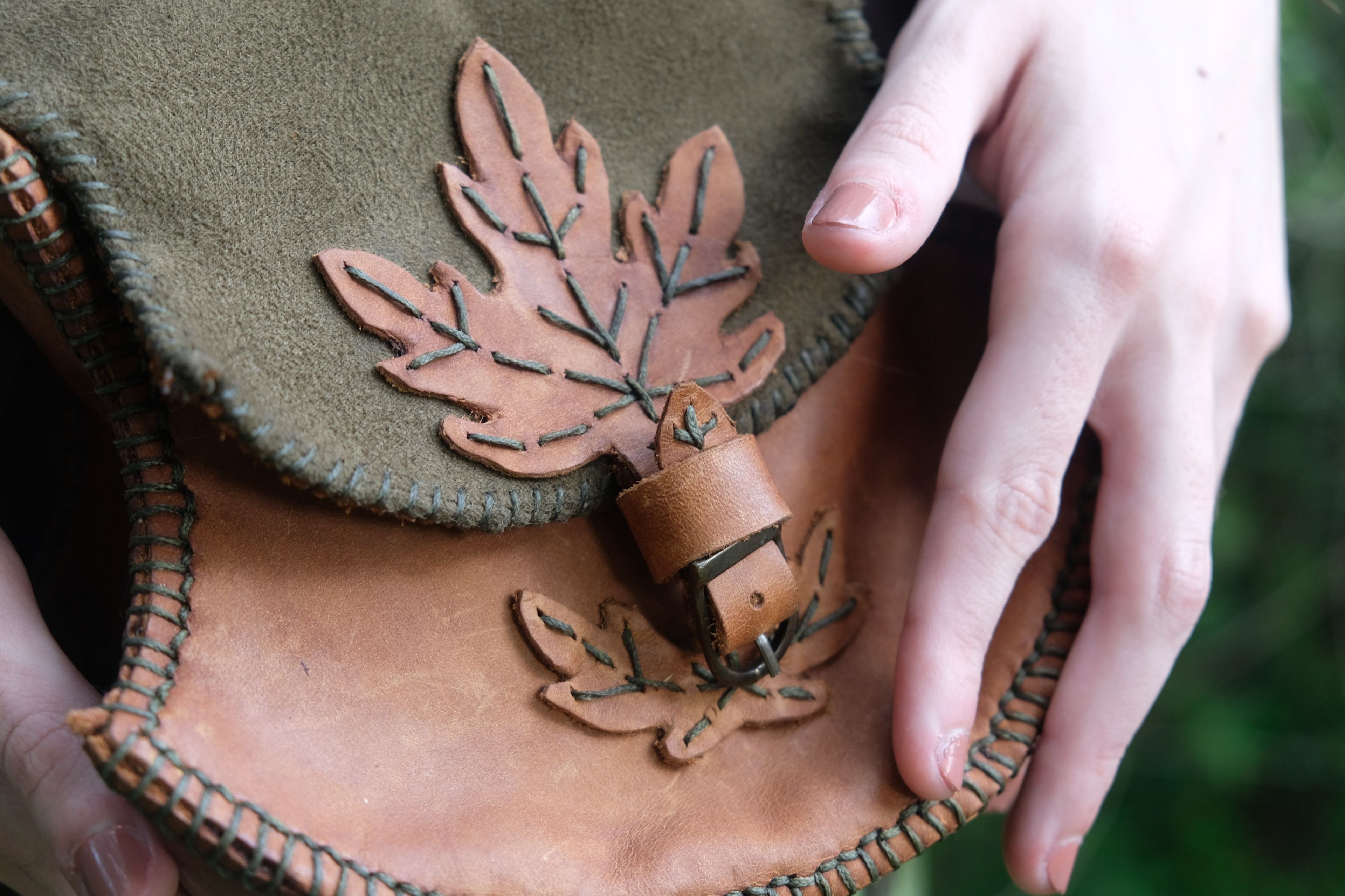 Hand on a green and tan leather pouch with a cut-out maple leaf