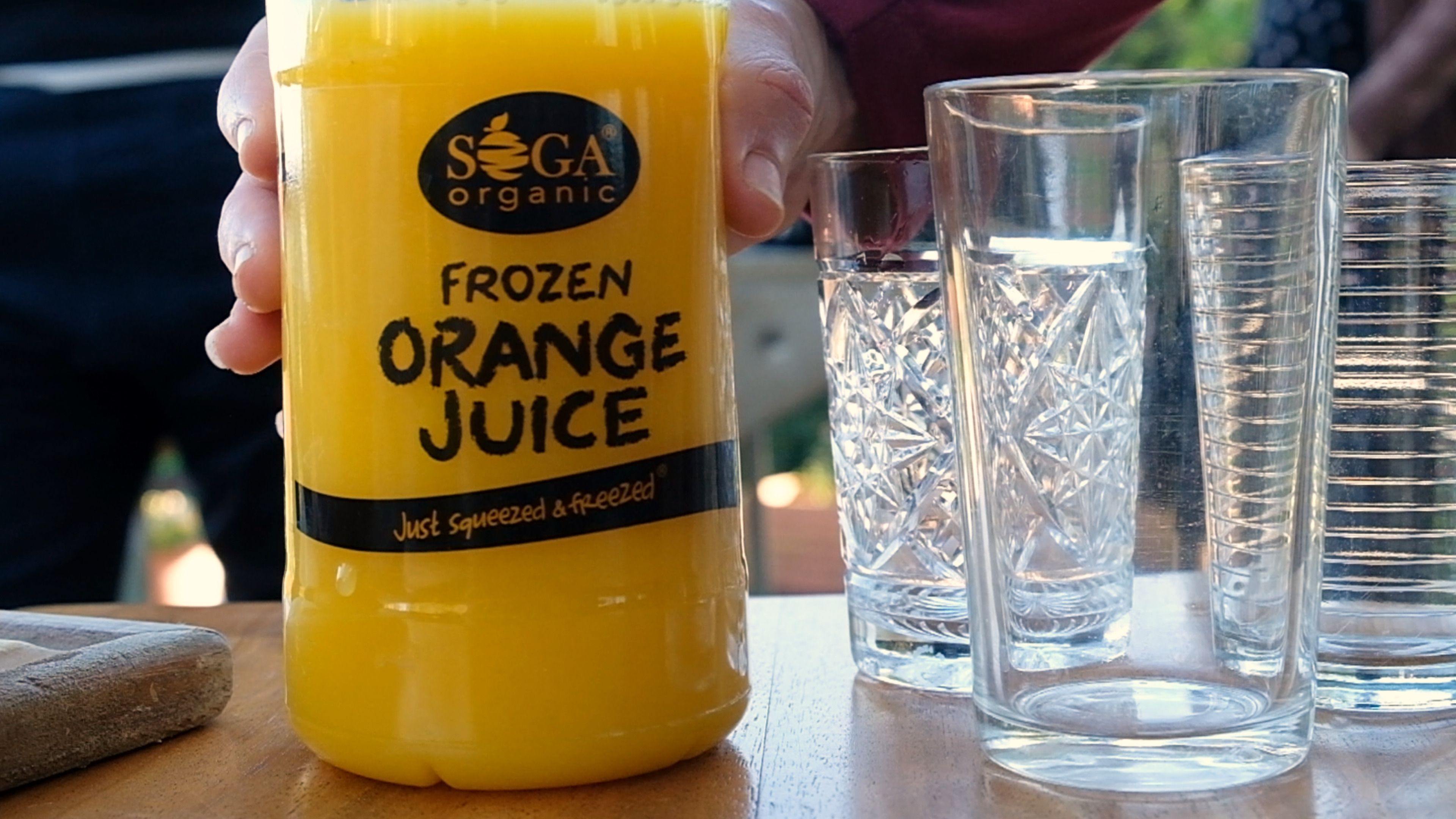 SOGA frozen orange juice bottle beside empty glasses on a wooden table