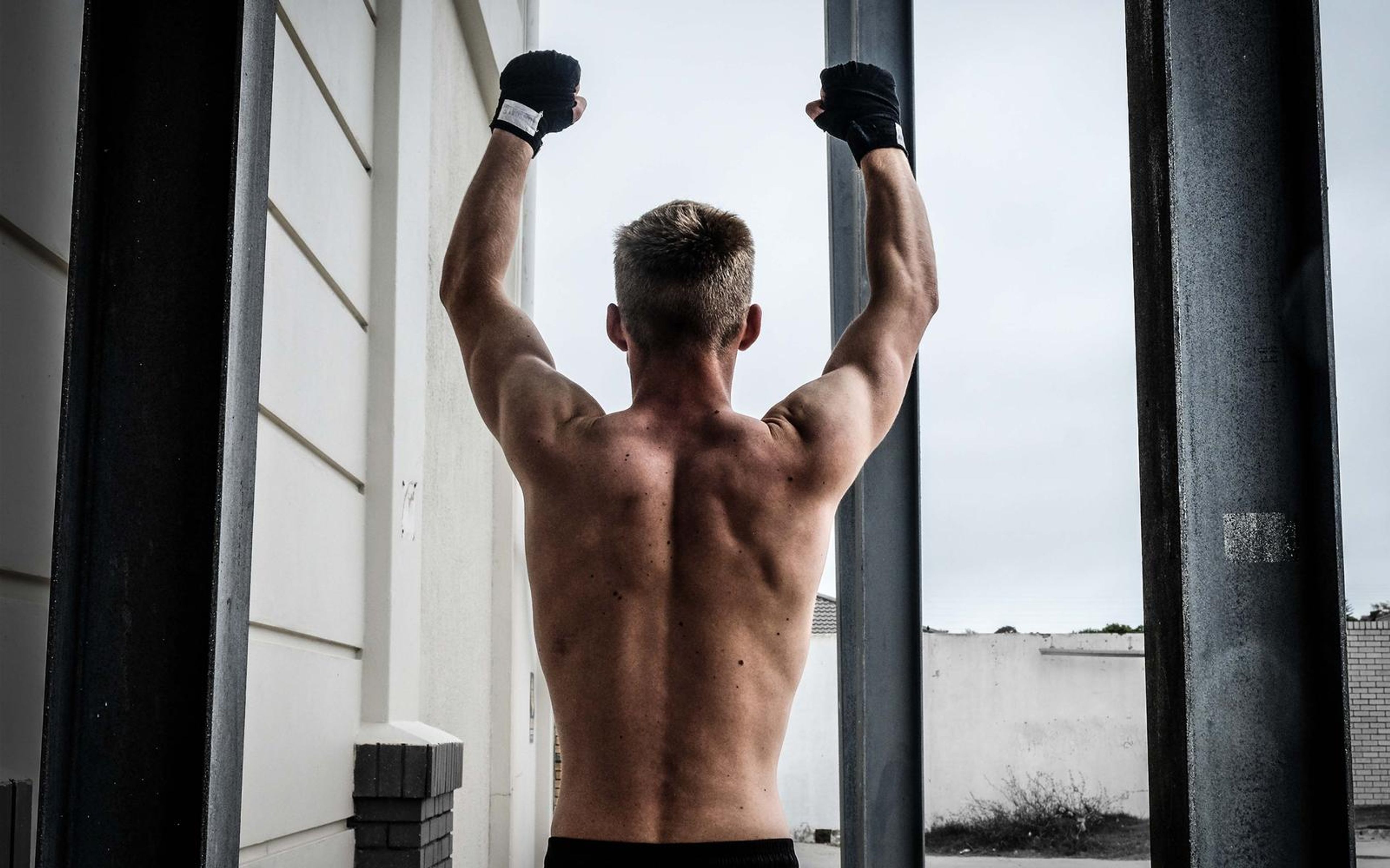 Man seen from behind with both wrapped fists raised, standing between steel posts