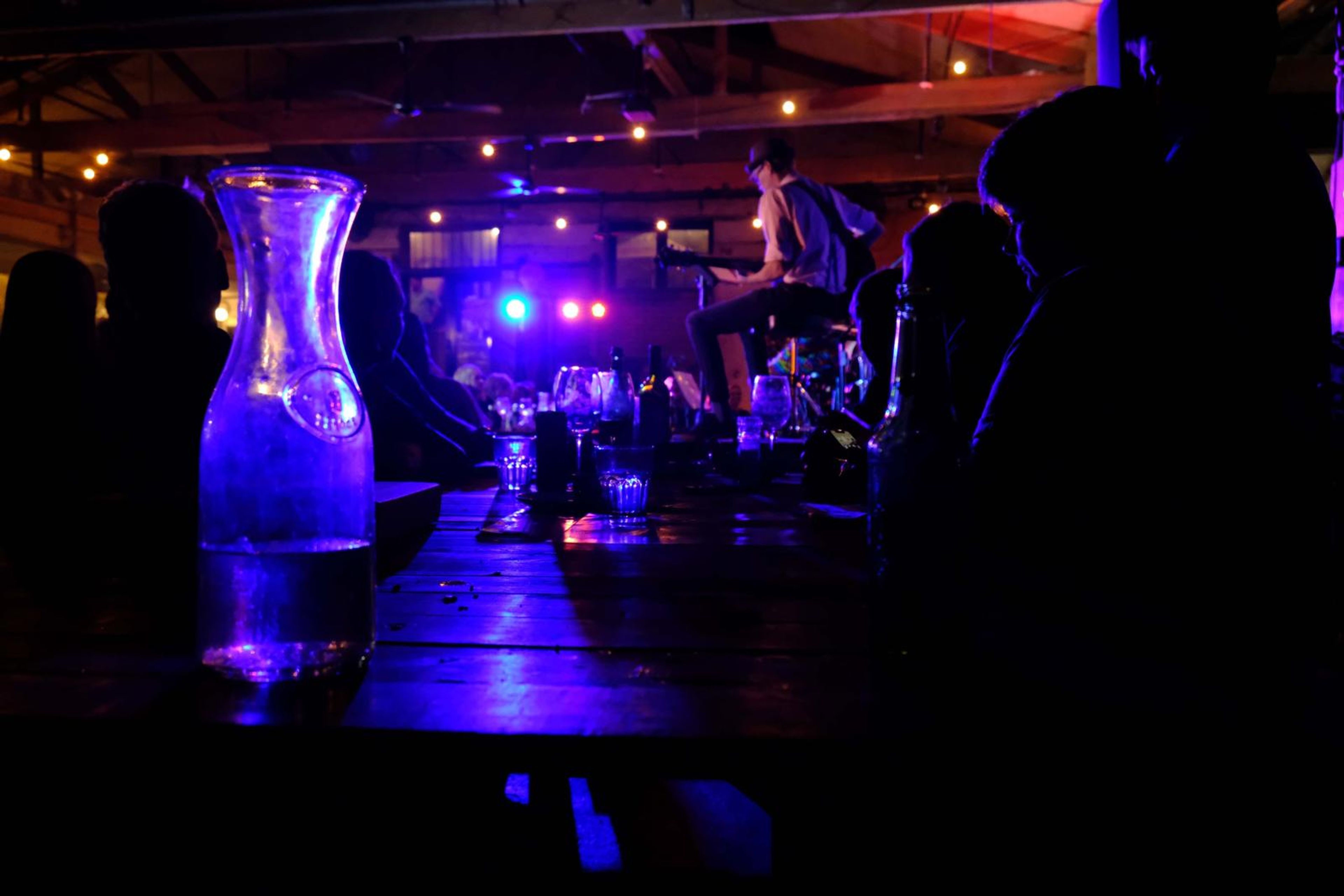 Glass carafe on a table glowing purple against the stage lights