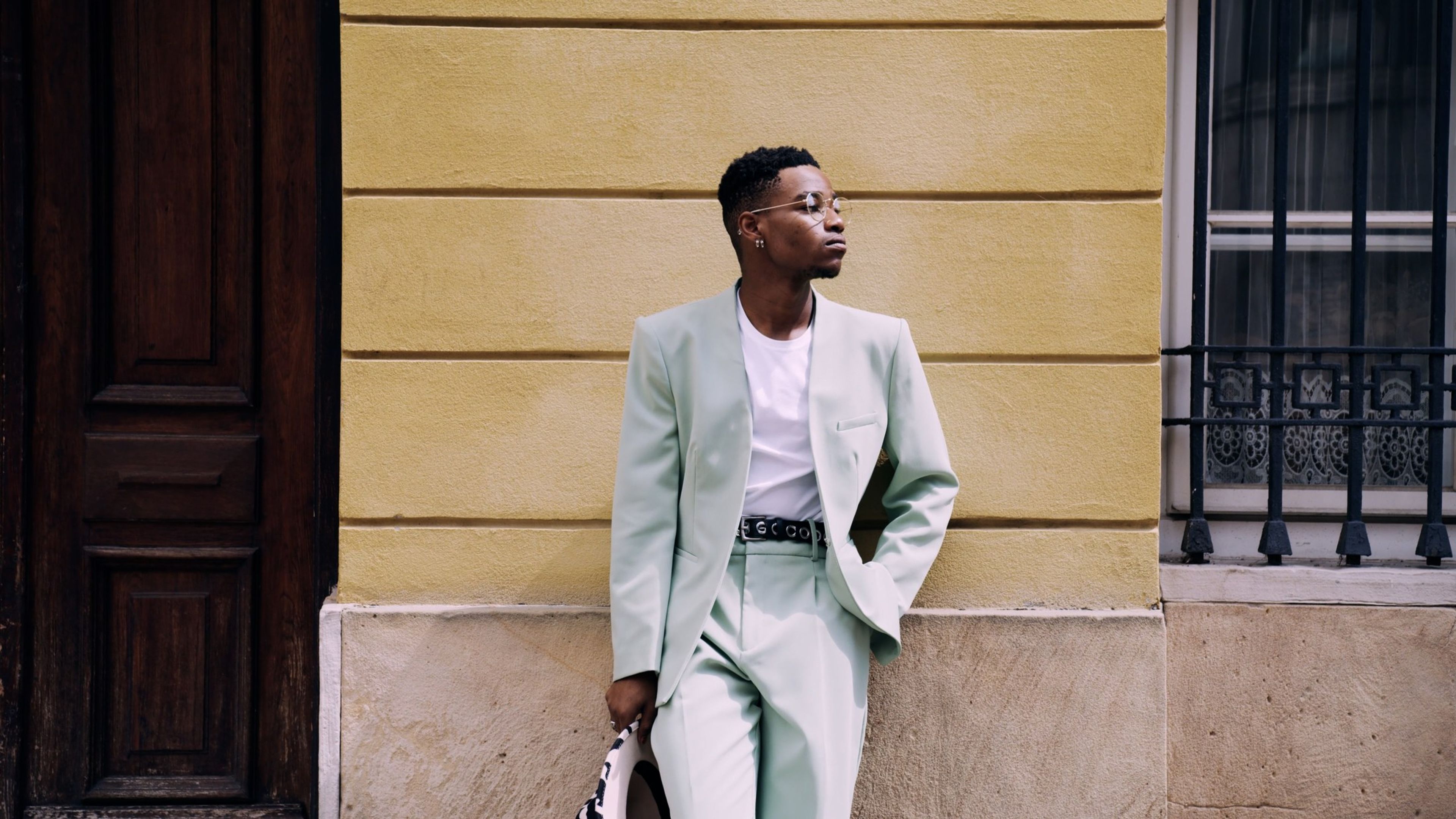 Man in a pale green suit standing in front of a wooden door