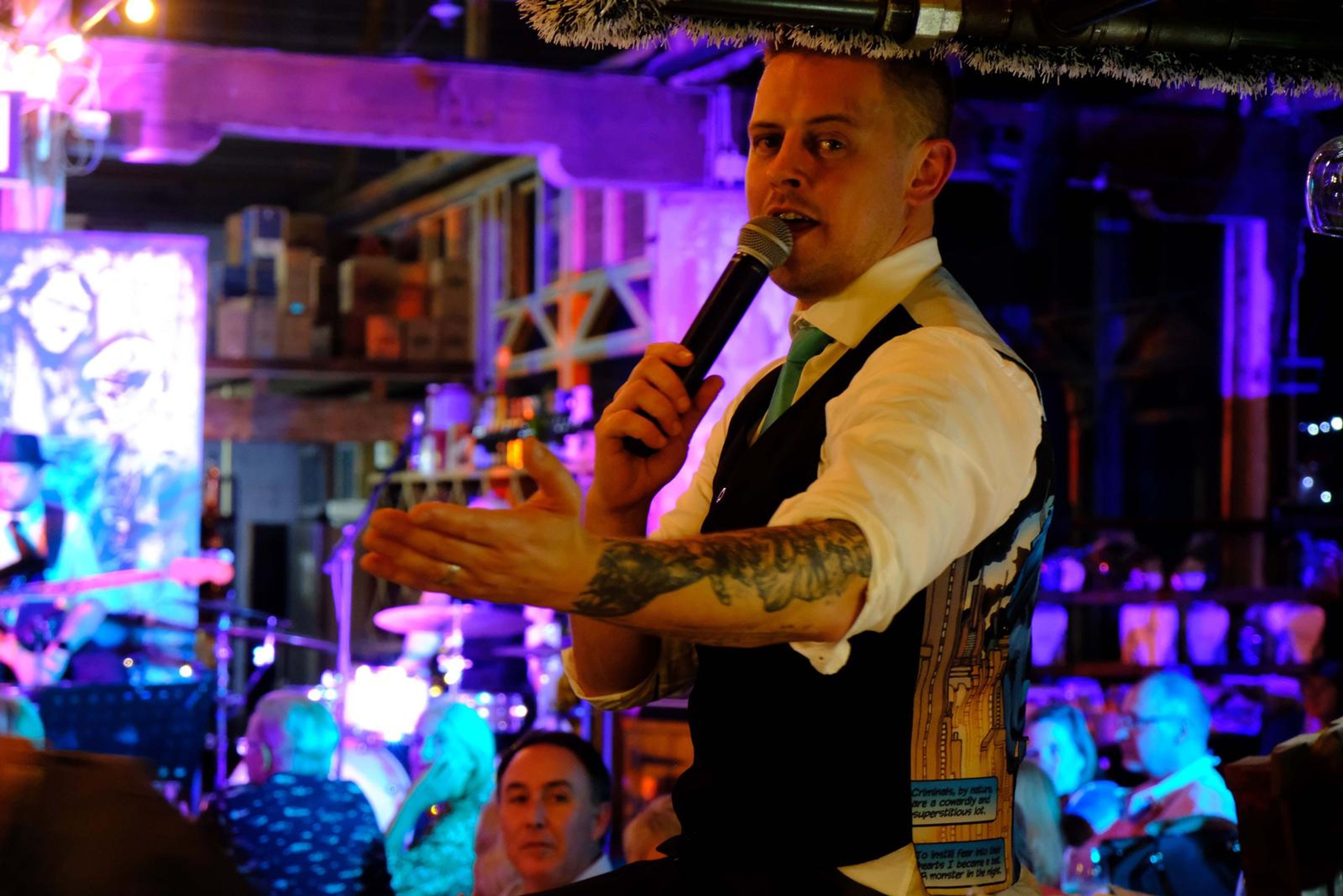 Singer in a waistcoat gesturing with an open hand to the crowd