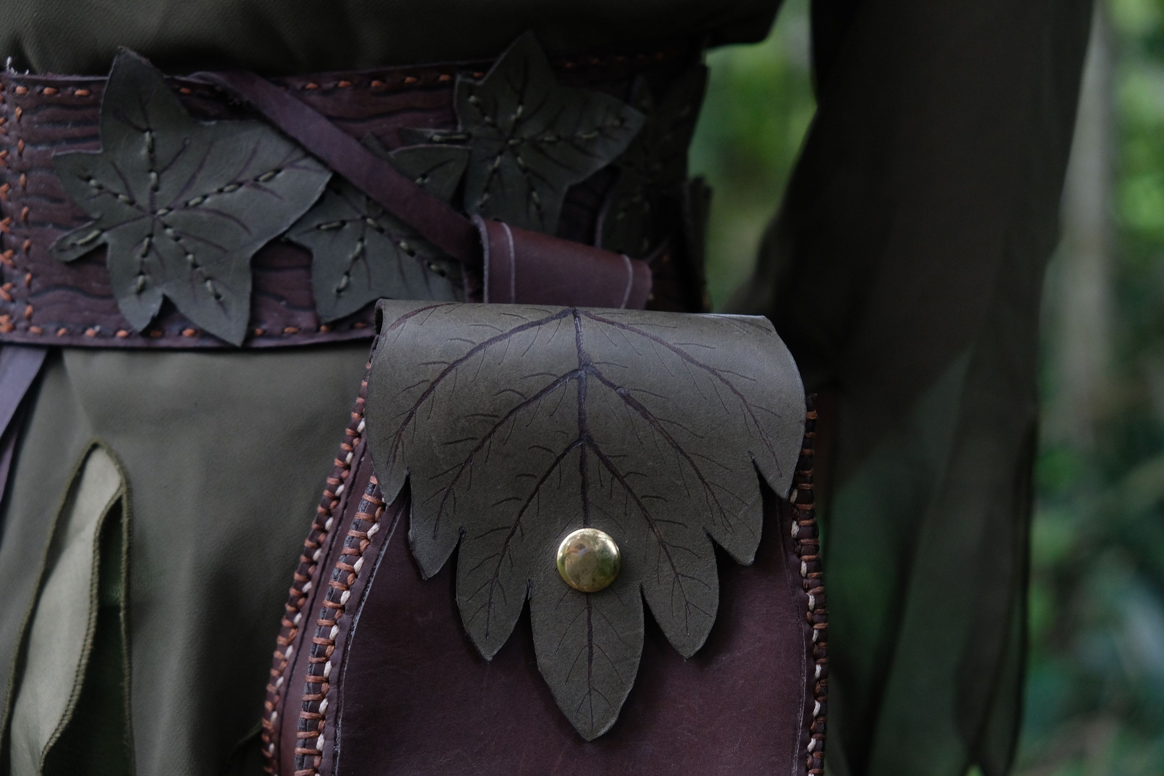 Close view of a purple leather belt and a bag with an embossed leaf flap