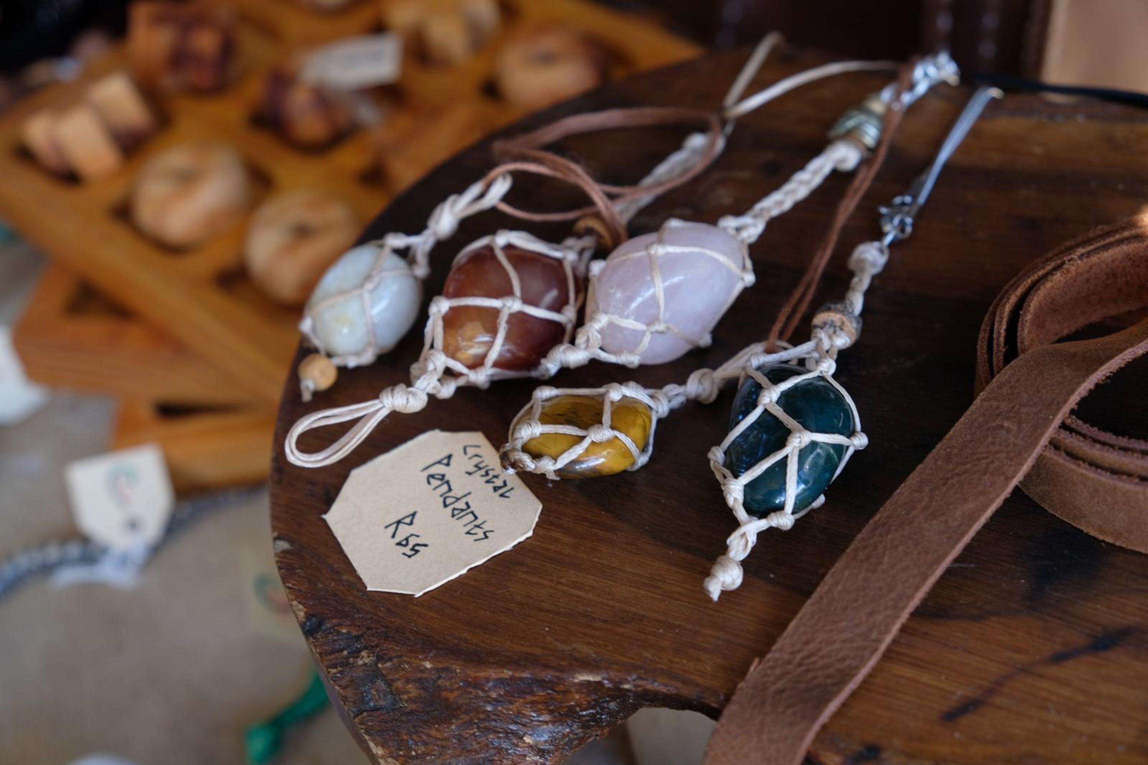 Wire-wrapped crystal pendants on a wooden stool beside a leather strap