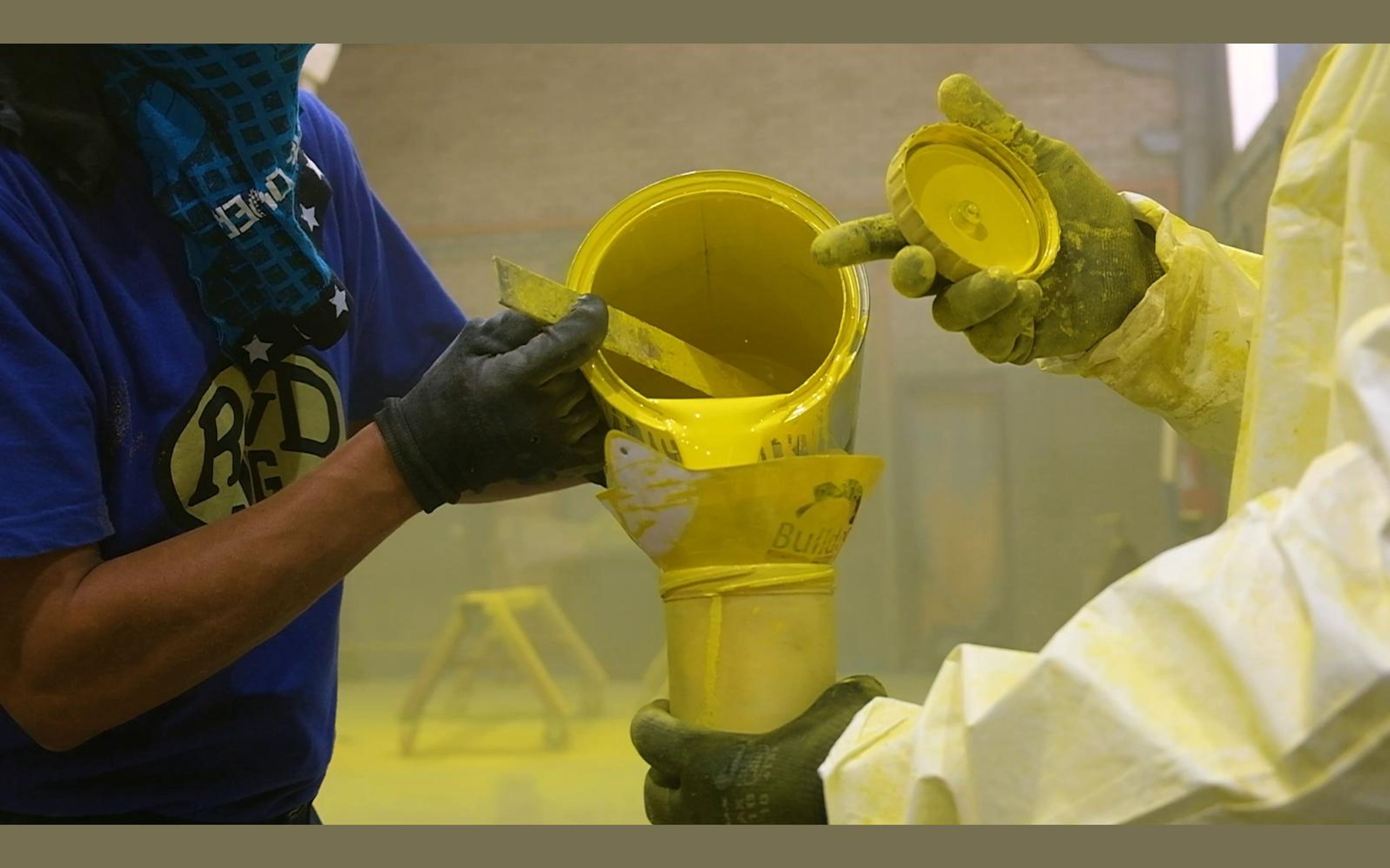 Painter in a respirator pouring yellow paint into a spray cup