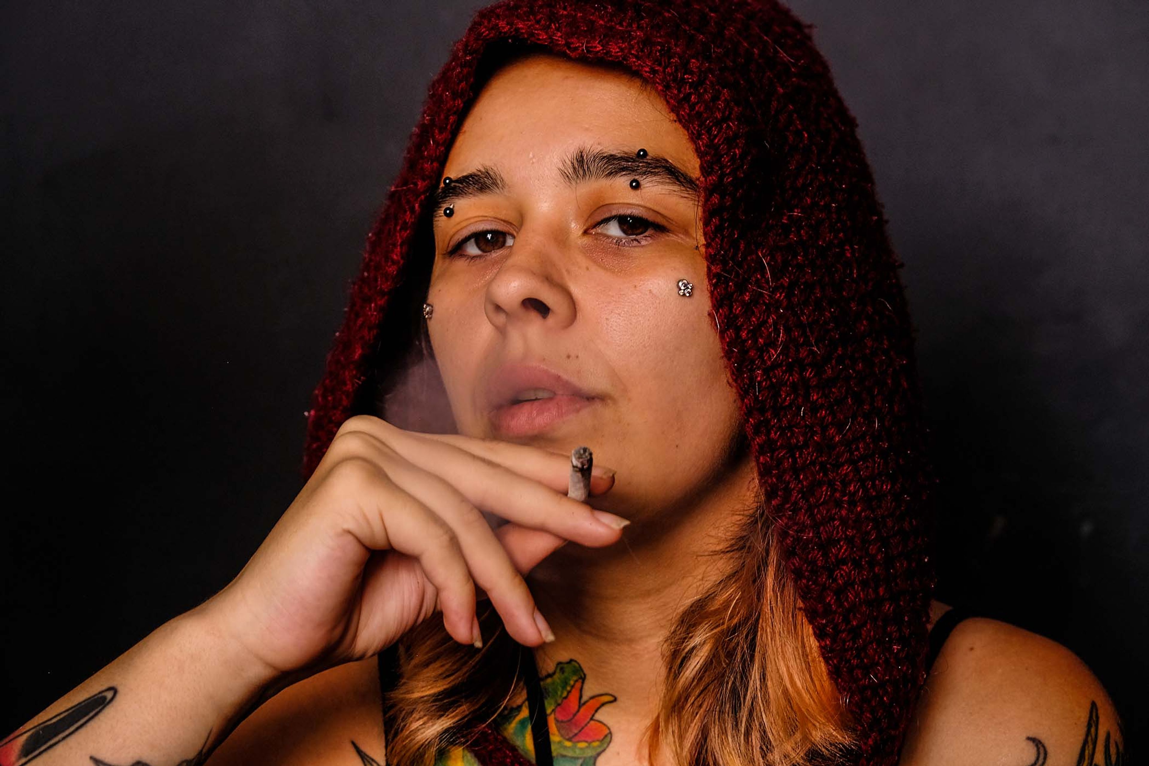 Close-up portrait, subject in a maroon knit hood resting chin on hand, cigarette smoke drifting past the face