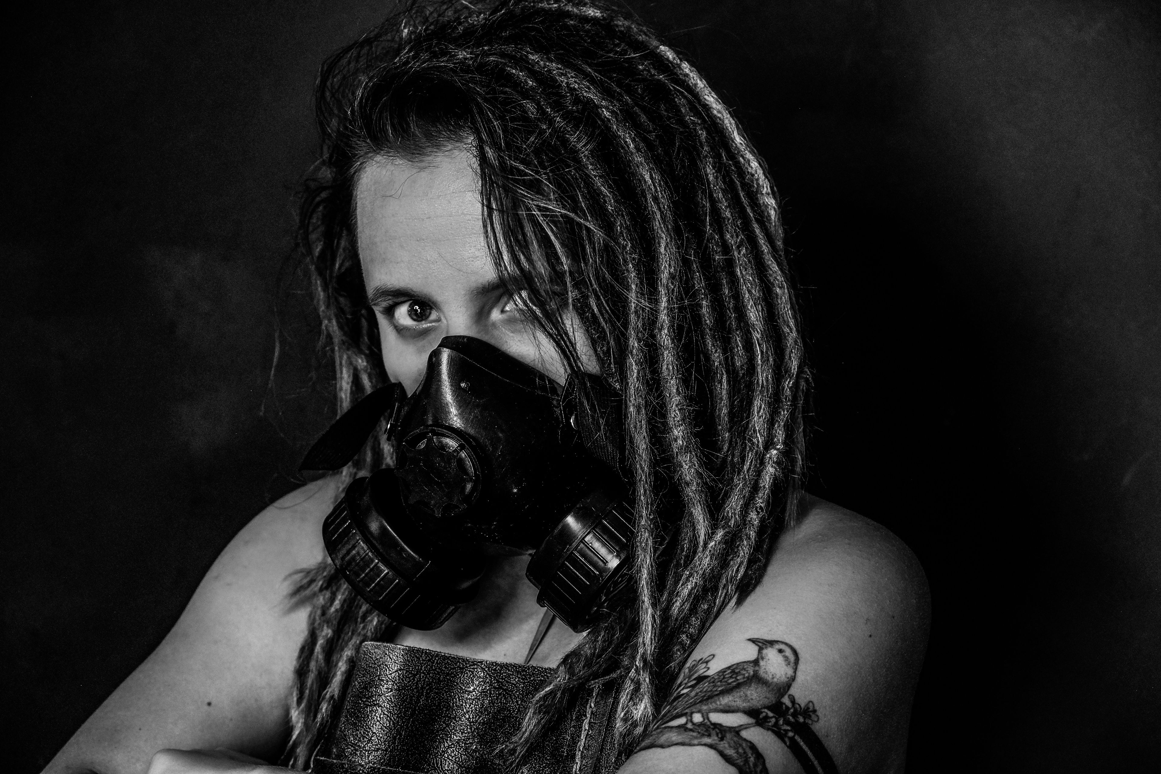 Black and white close-up portrait, subject wearing a gas mask, dreadlocks parted over one eye