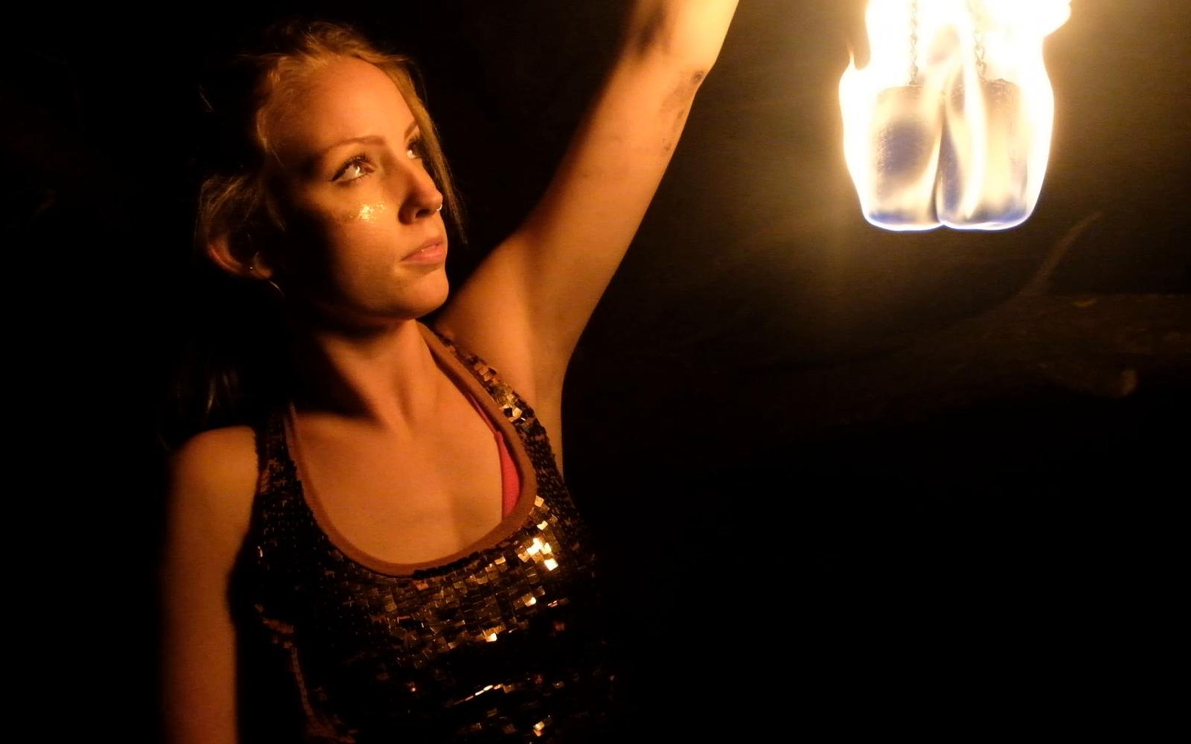 Woman in a sequinned top holding a flaming prop above her head and looking up