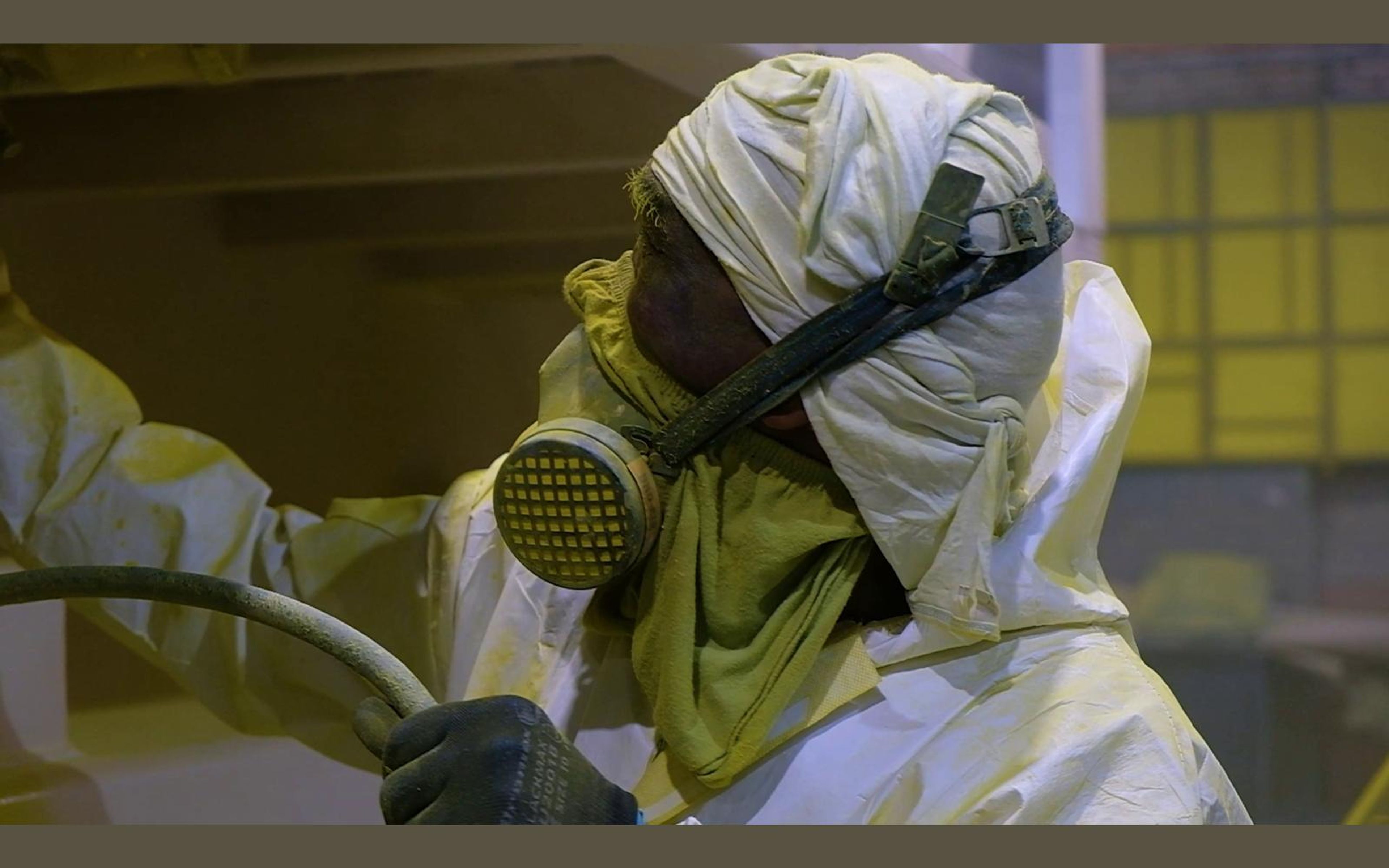 Painter in a hood and respirator holding a spray gun