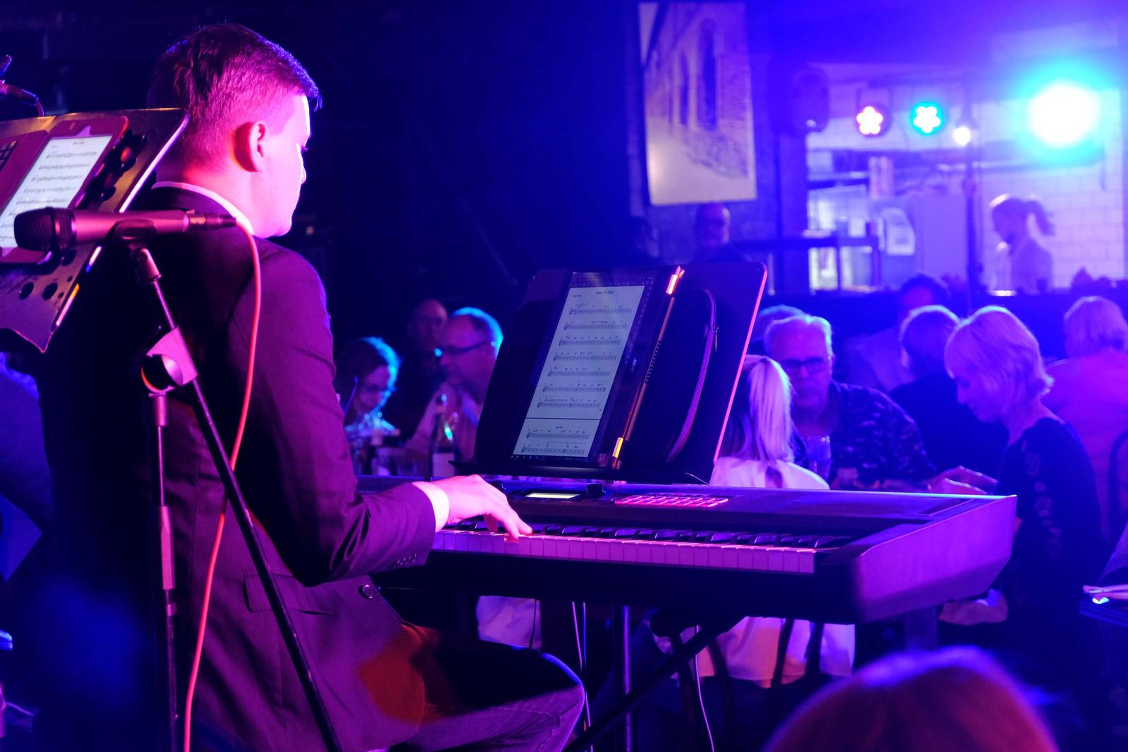 Keyboard player in a suit at the piano with the restaurant behind