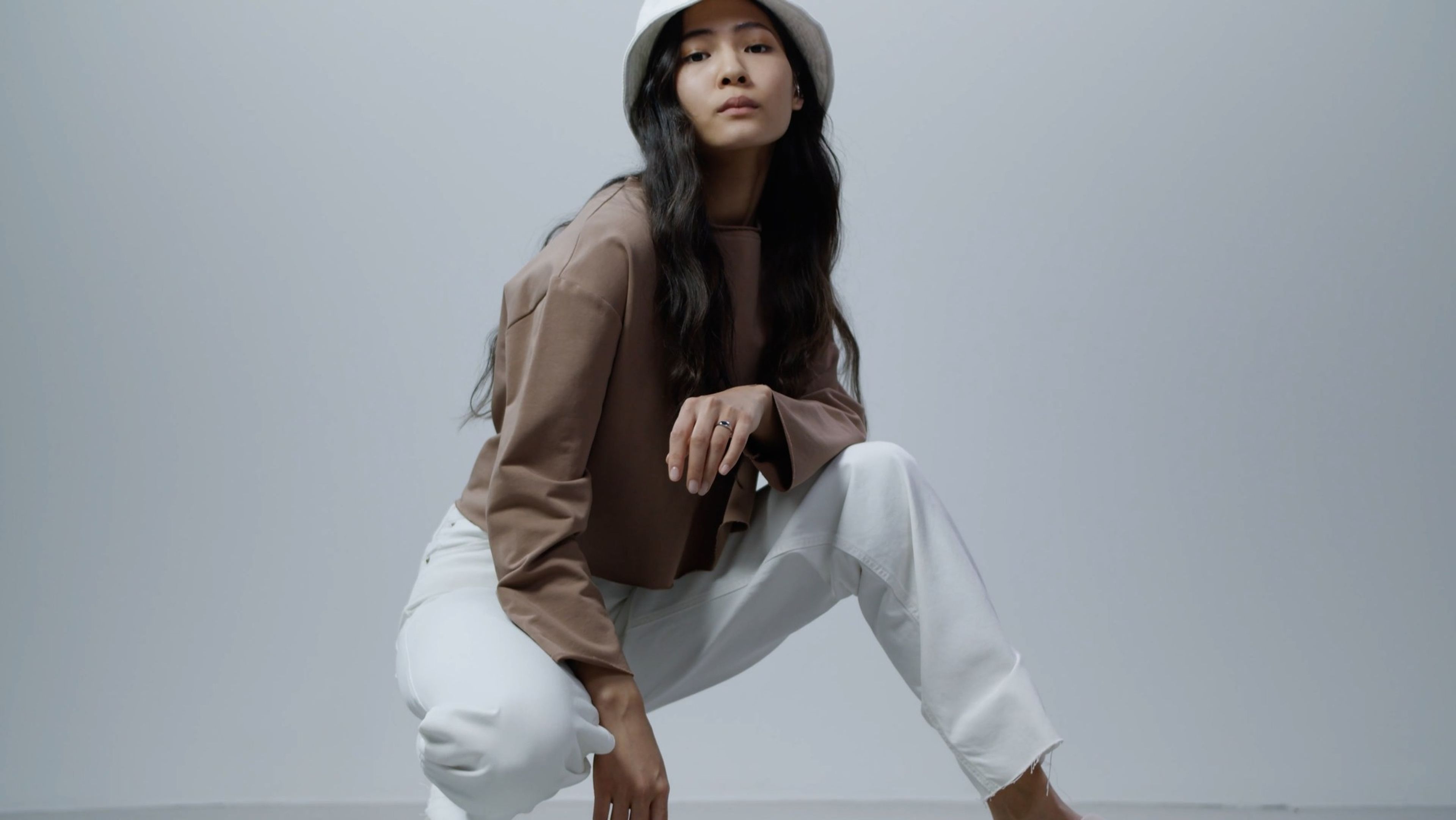 Woman in a bucket hat and brown jacket posed against a pale blue backdrop