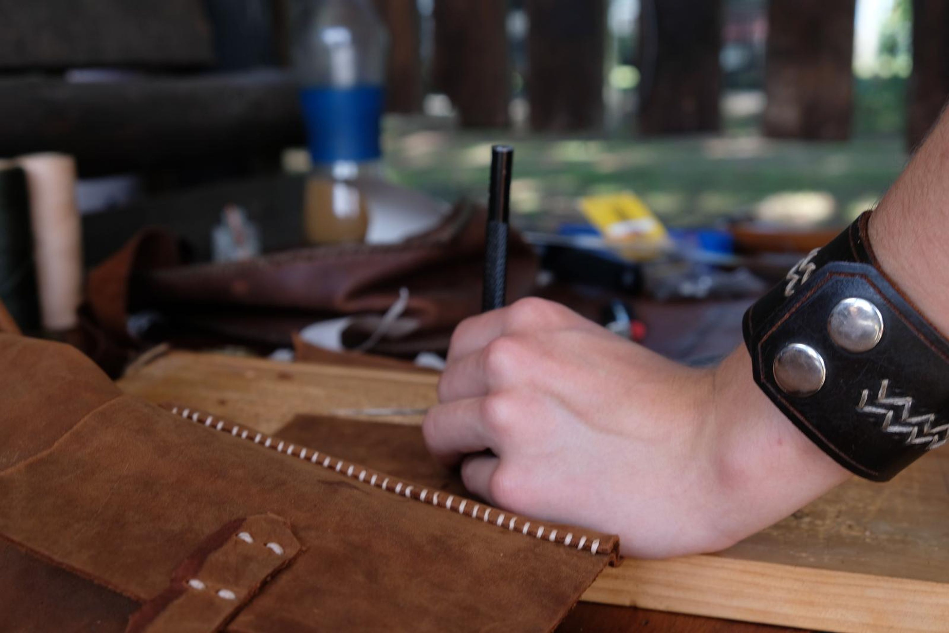 Hand marking stitch holes along a leather piece on a wooden board