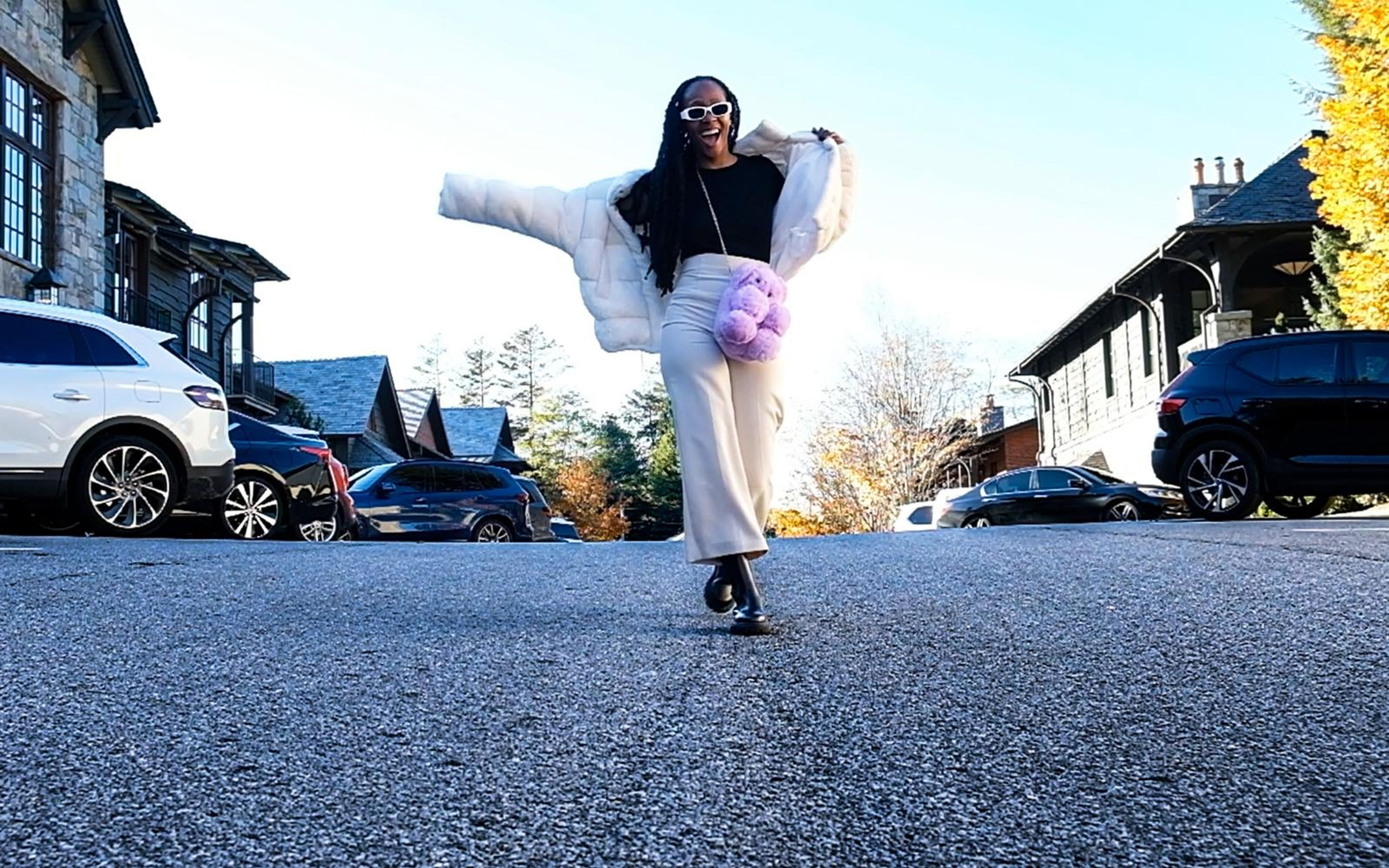 Model with arms swung out in a wide stance on the road, white fur jacket, purple bag, low angle