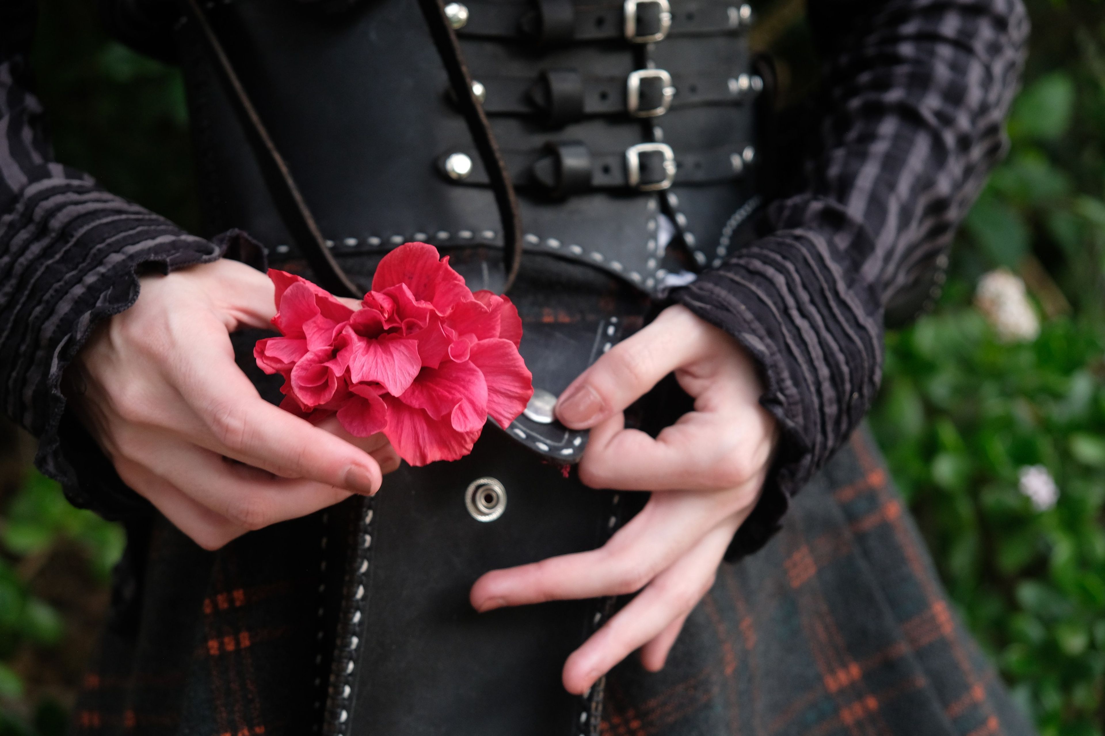 Hands placing a red flower into a black leather pouch above the corset belt