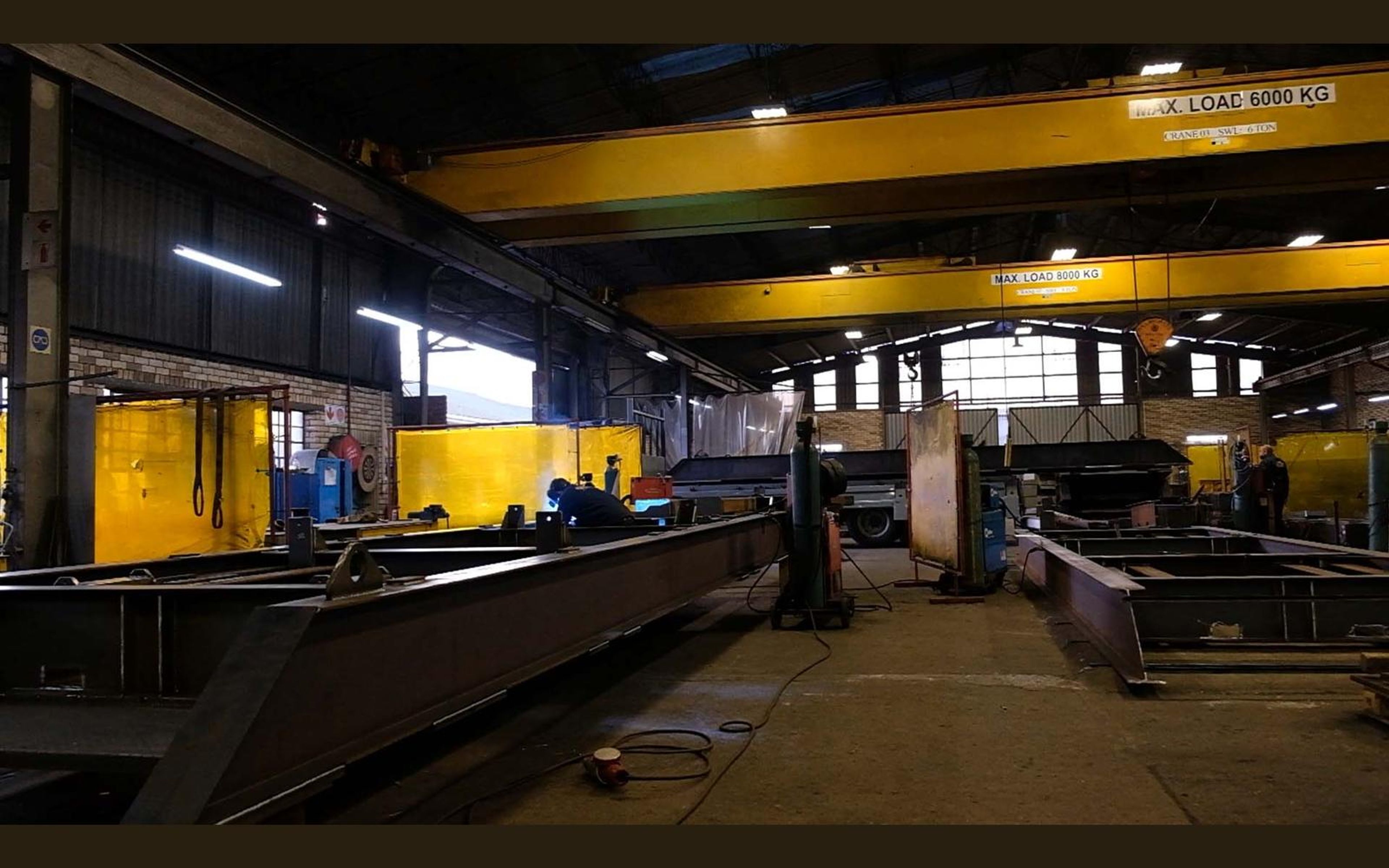 Fabricators at work among steel beams in the shop