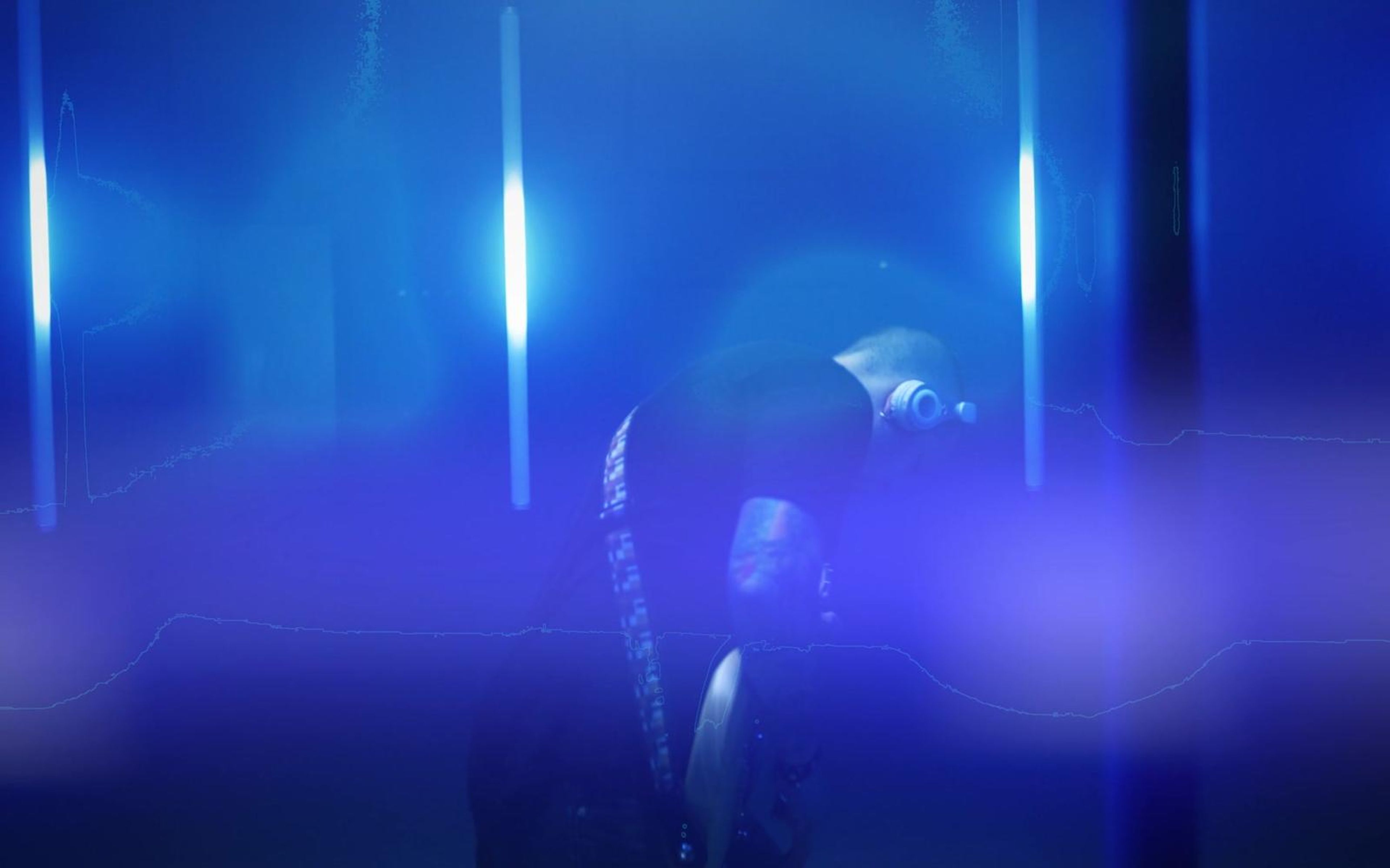 Guitarist silhouetted in saturated blue and violet light with a glowing vertical tube behind