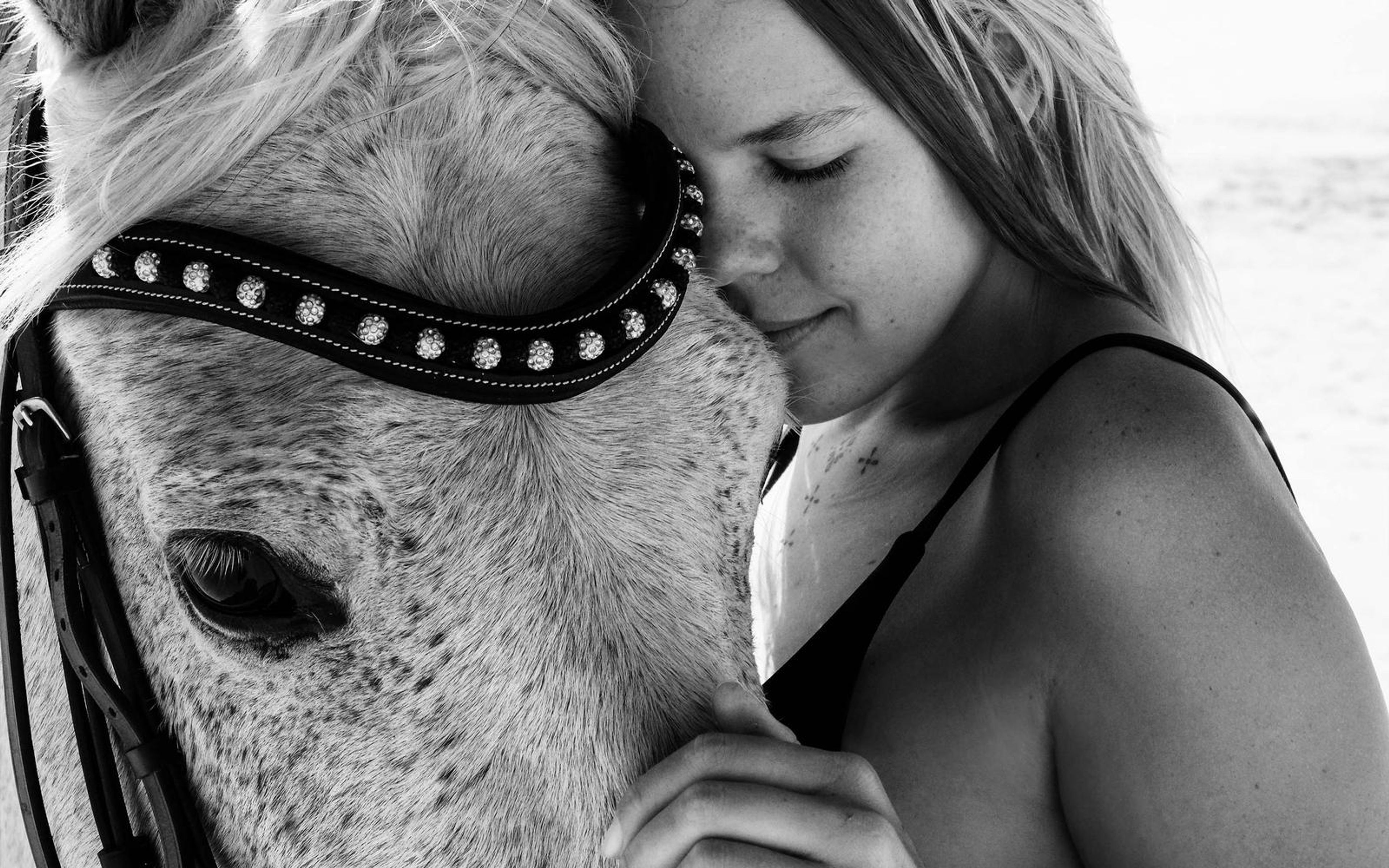 Black and white close portrait of a woman with bare shoulders resting her cheek against a horse, hand on its muzzle