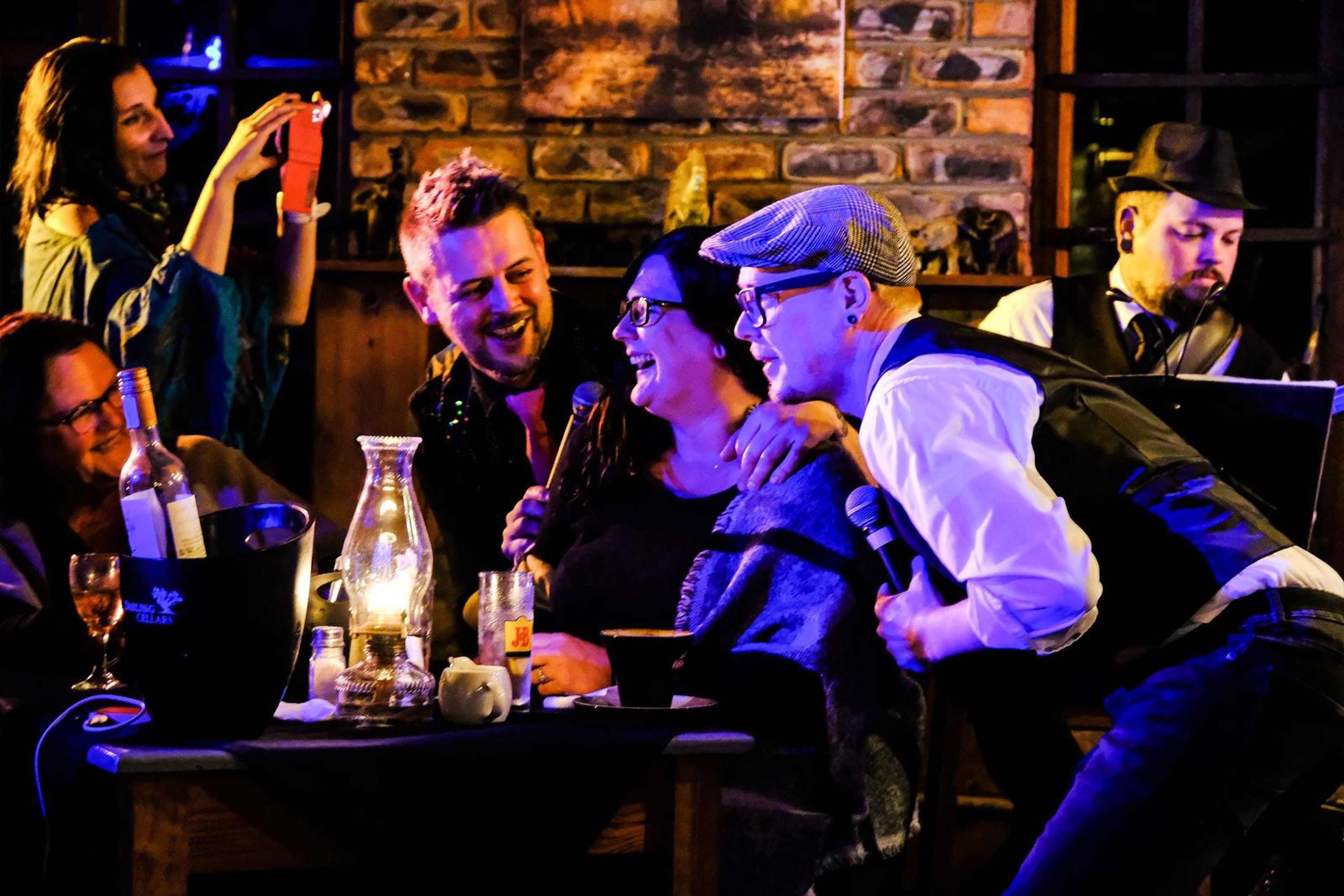 Guests laughing as two singers lean in with a microphone at their table