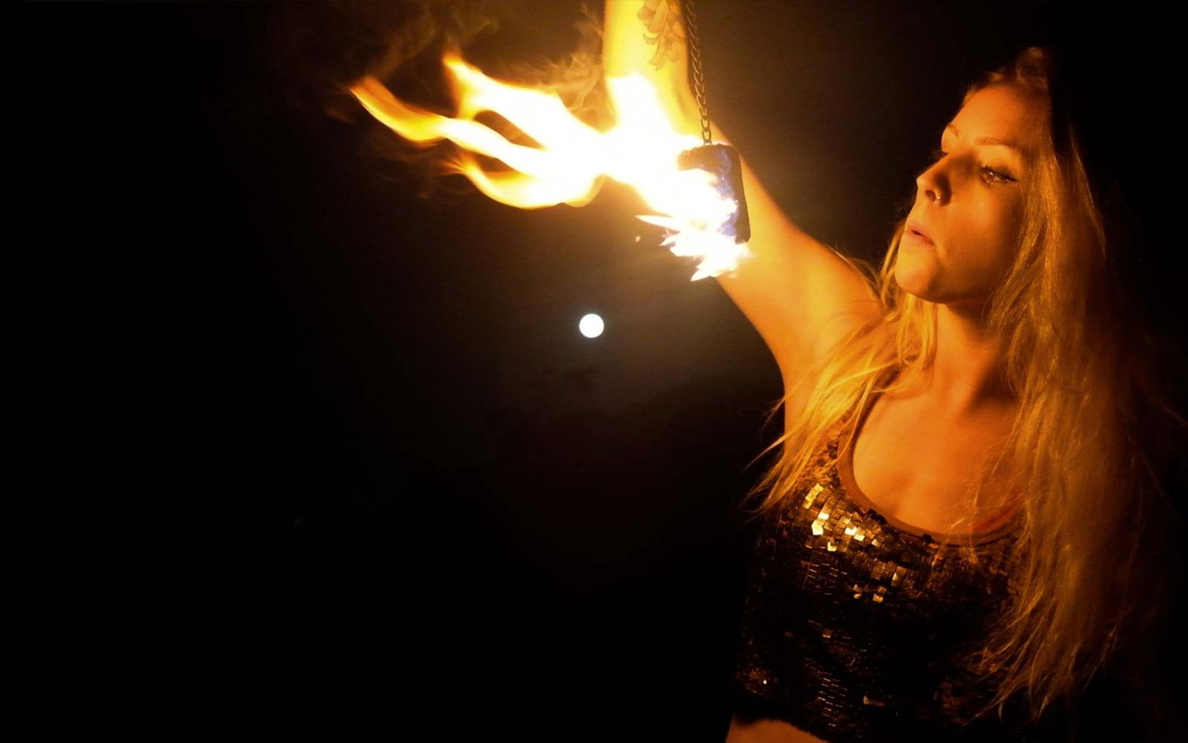 Woman in a sequined top raising a flaming prop above her head, bright flame at the top left