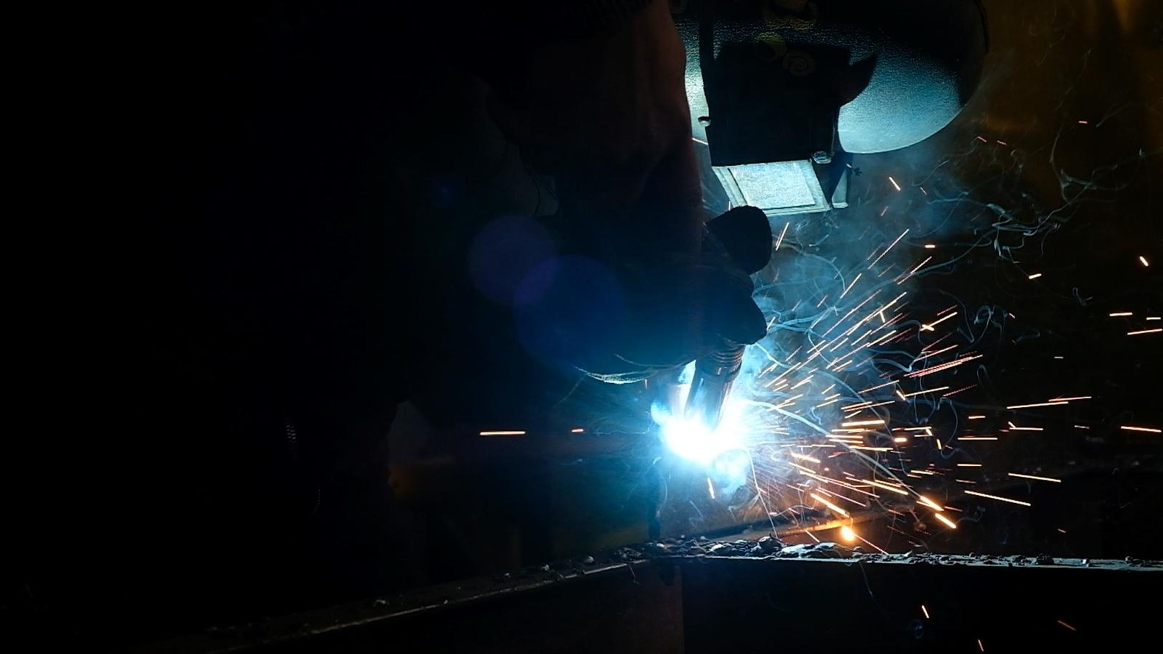 Welding arc flaring with sparks beside a helmeted welder