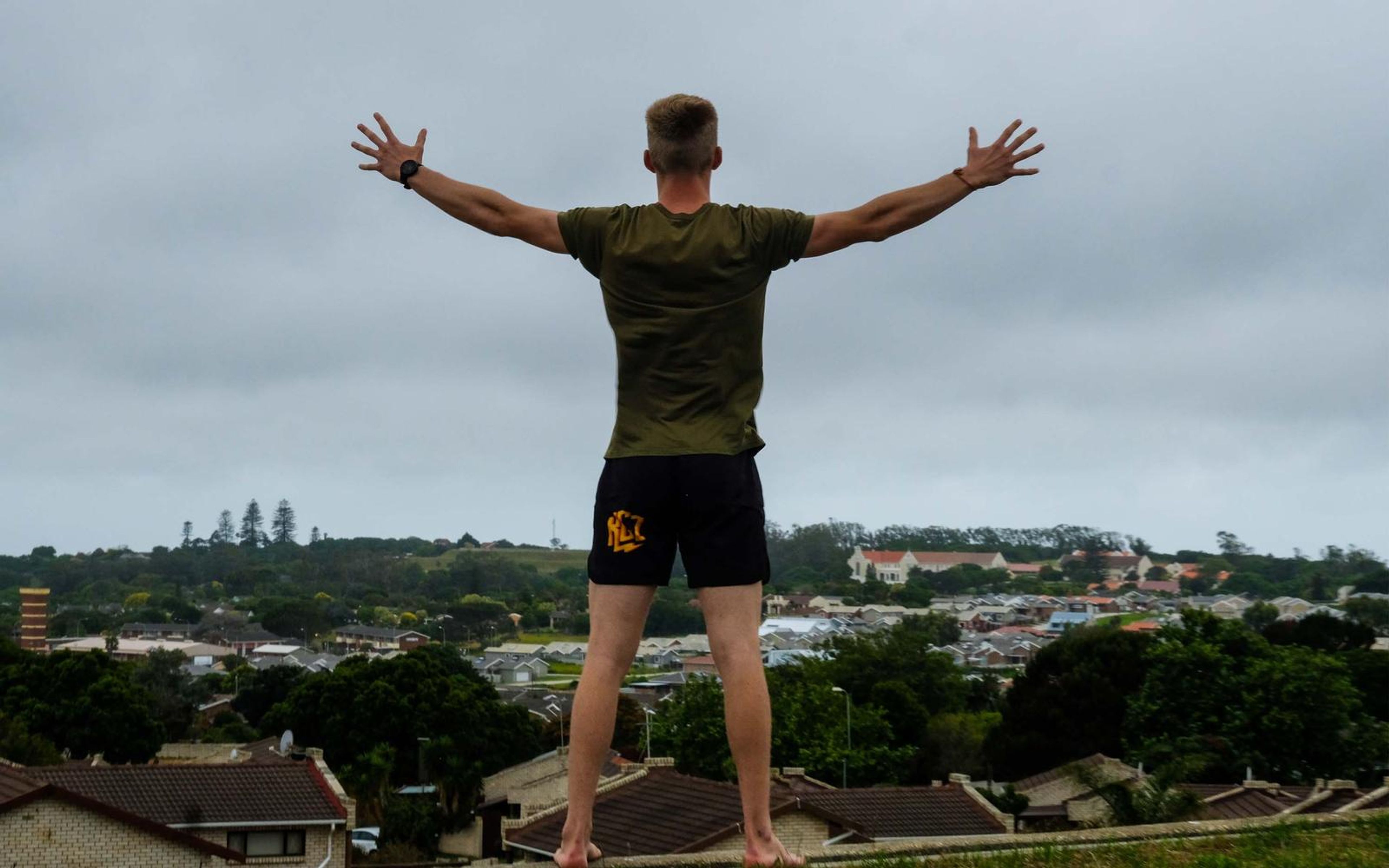 Fighter from behind on a grassy hill with arms spread wide under a grey sky
