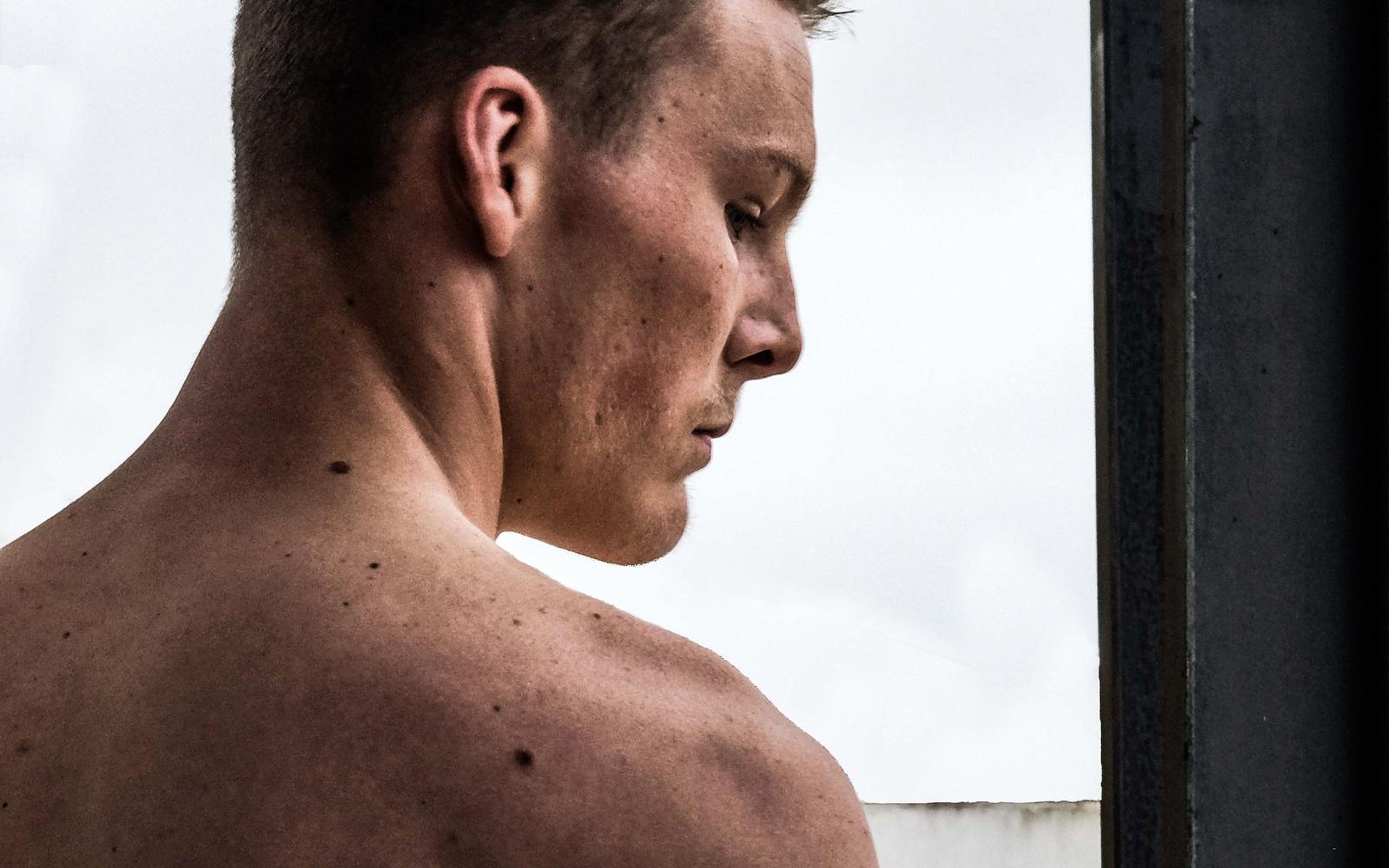 Close crop of a man's head turned down over his shoulder against a white sky