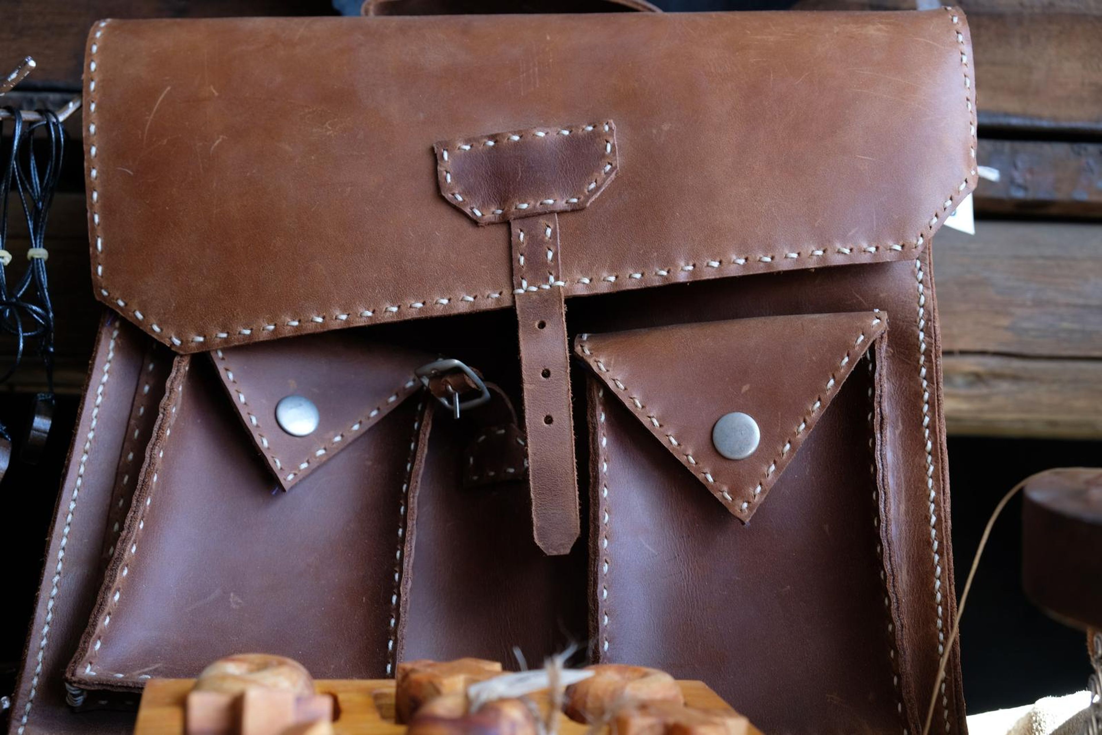 Close-up of a hand-stitched brown leather satchel with two buckled pockets