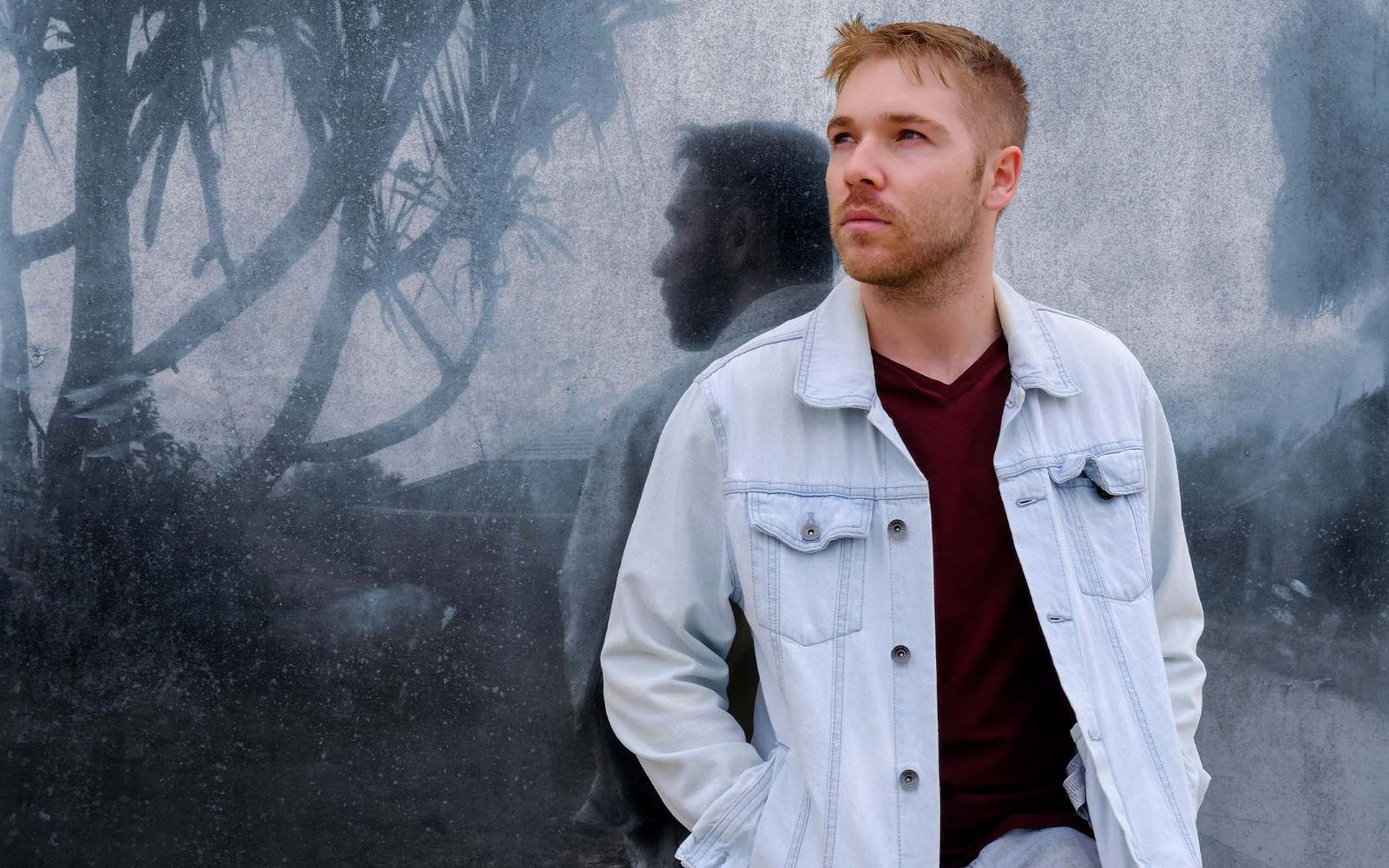 Portrait of a man in a light denim jacket and maroon tee in a blue-toned frame, ghosted double exposure behind
