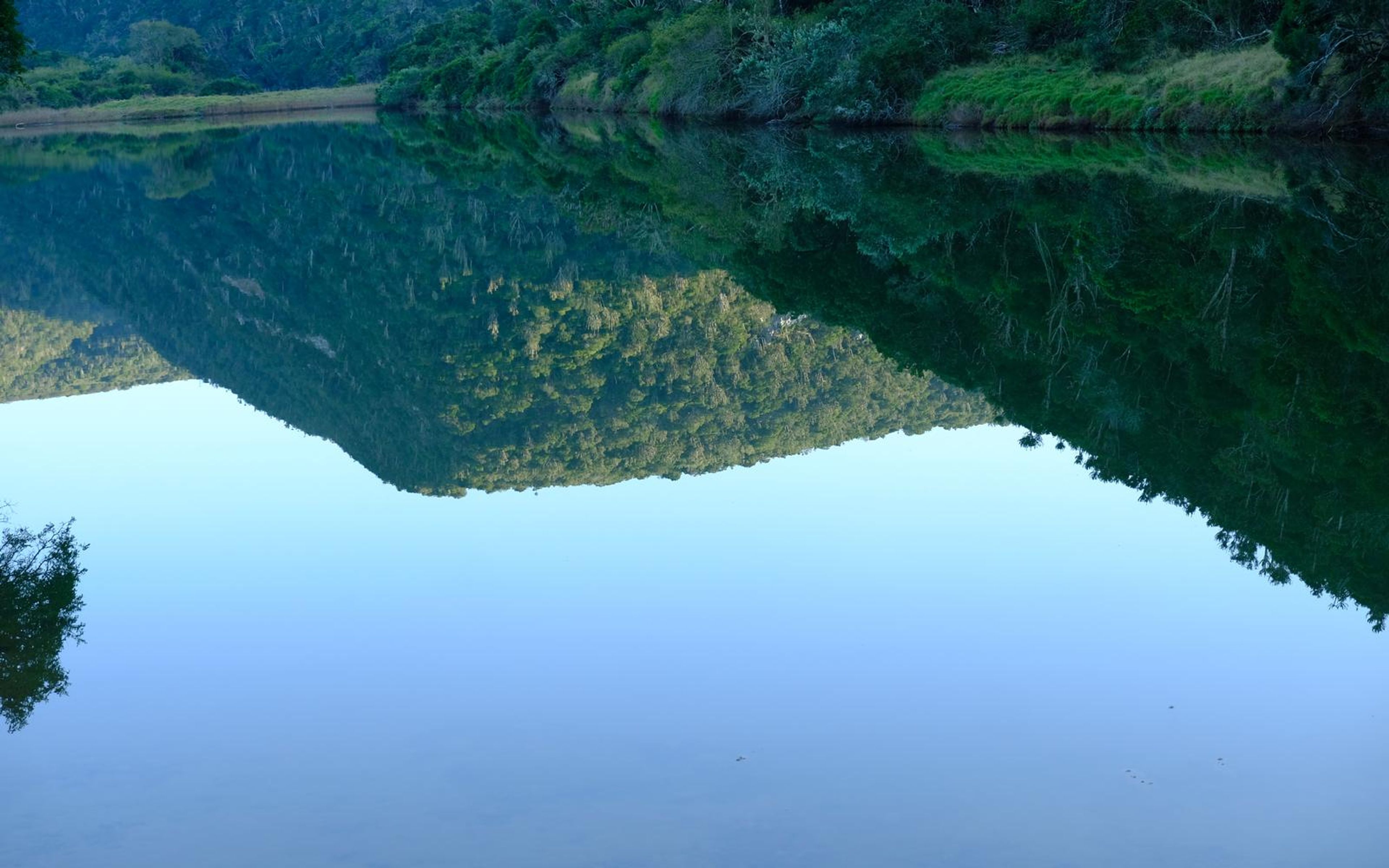 Close crop of the reflected hills and bank, the water almost mirror smooth
