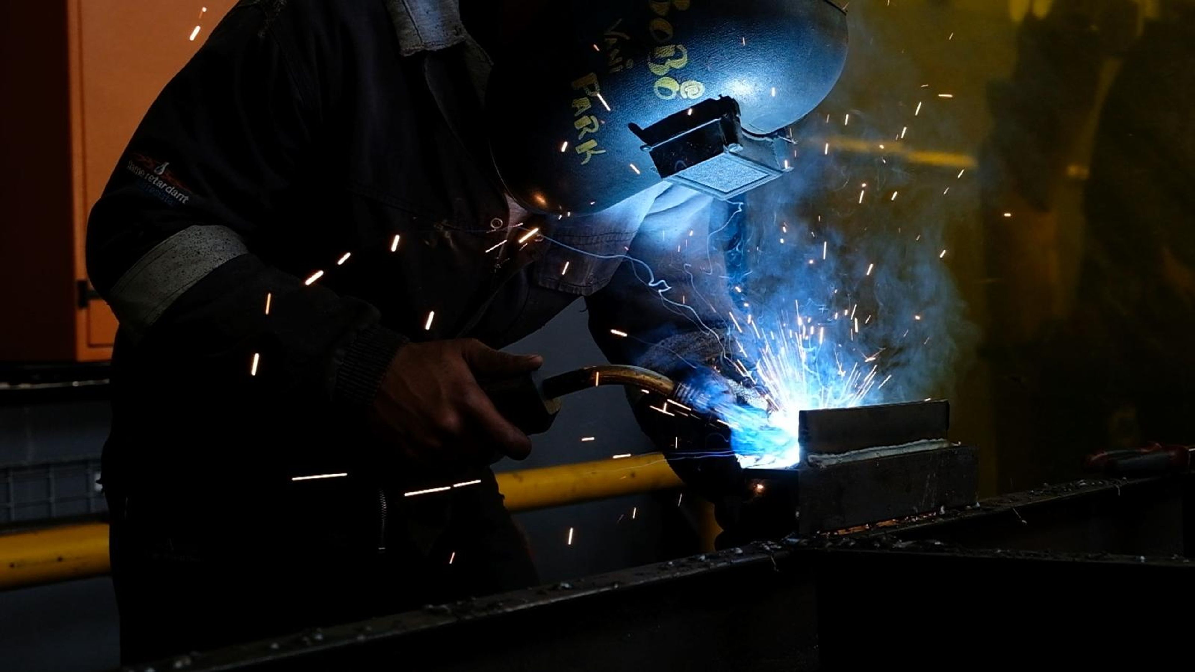 Welder in a helmet in a shower of blue light and sparks